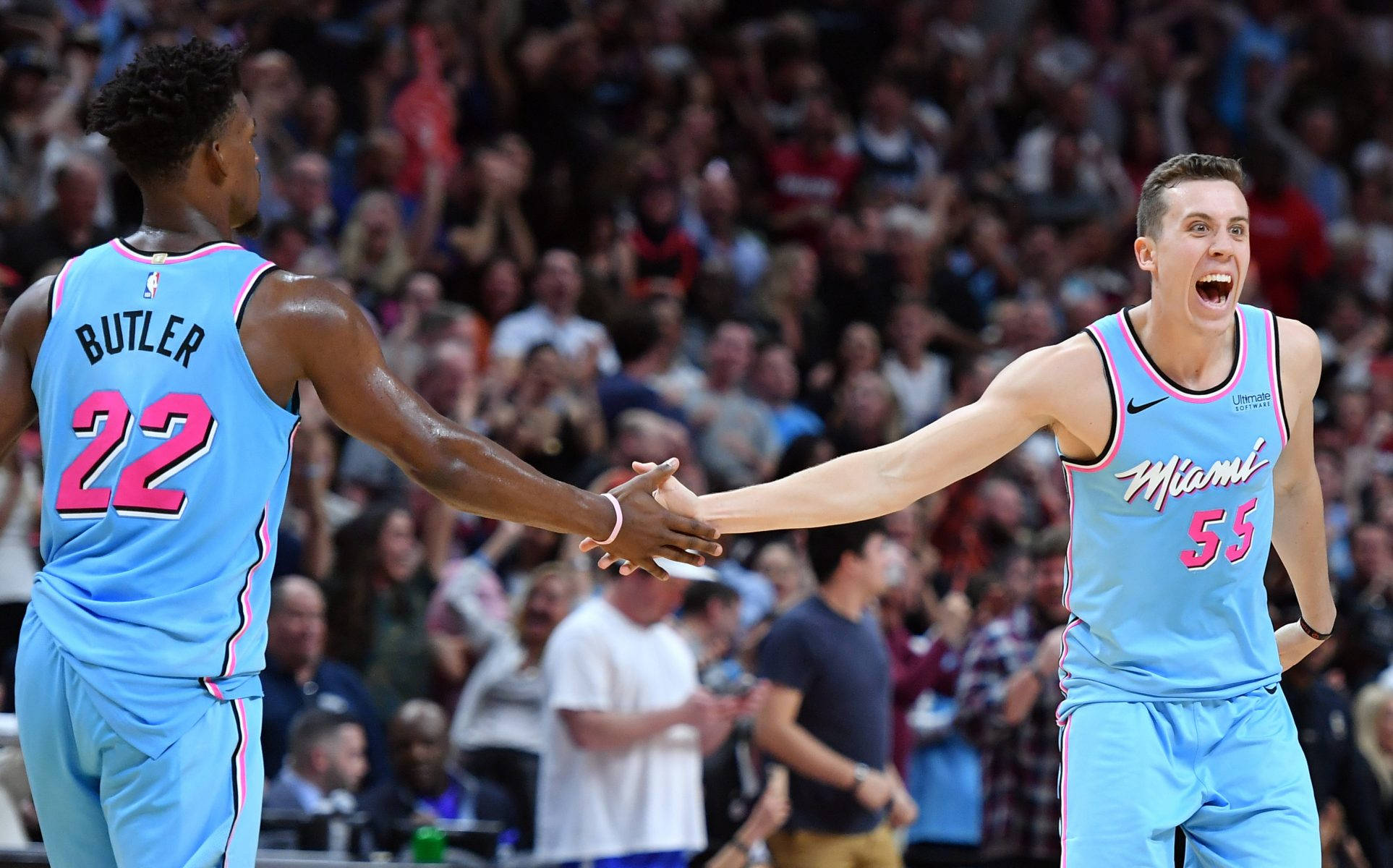 duncan robinson 桌布 壁紙 — 兩位身穿淺藍色和粉紅色球衣的邁阿密熱火籃球運動員在比賽中擊掌慶祝，背景是歡呼的人群。