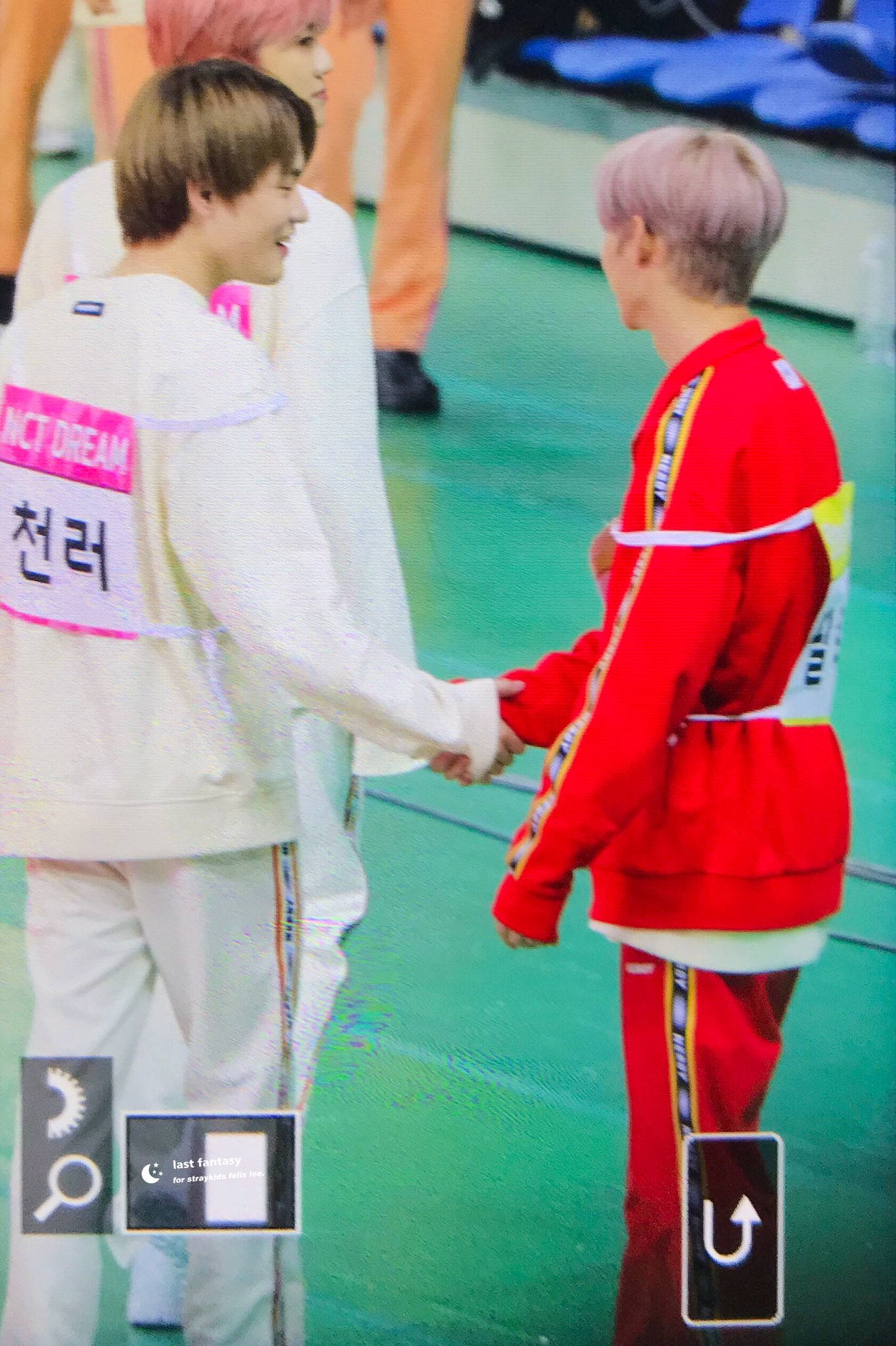 Stray Kids 桌布 壁紙 — 兩位身穿白色和紅色運動服的K-pop偶像在綠色舞台上握手，燈光明亮，背景模糊。