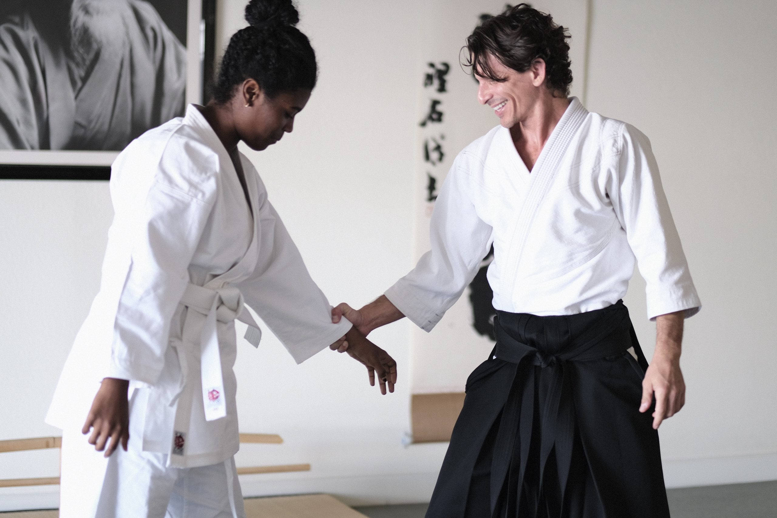martial arts 桌布 壁紙 — 兩位身穿白色和黑色道服的武術家在簡約的道場中，牆上有書法，互相恭敬地握手。
