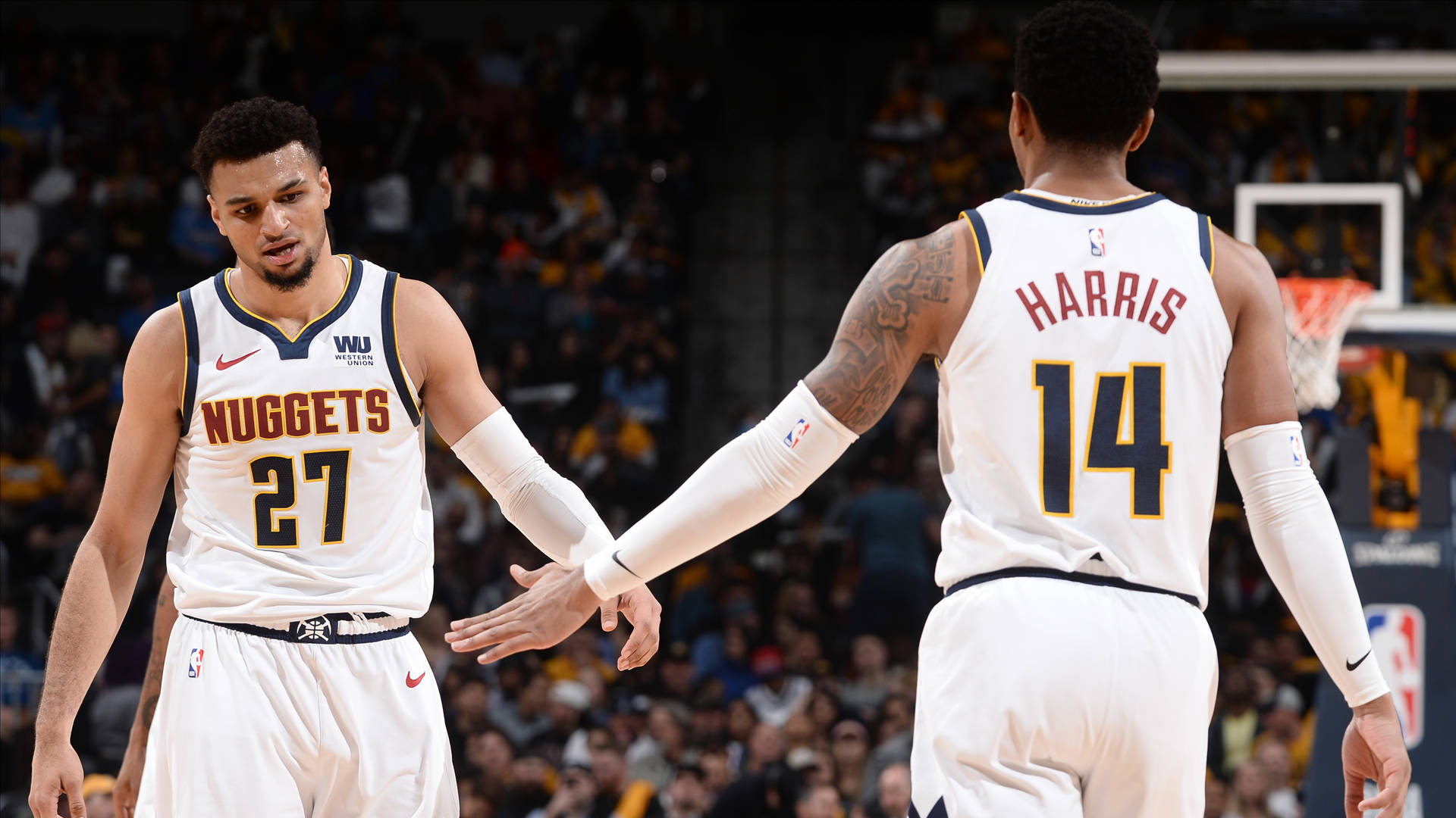 gary harris 桌布 壁紙 — 兩位身穿白色球衣的丹佛金塊籃球運動員在燈光明亮的球場上握手，身後是模糊的人群。