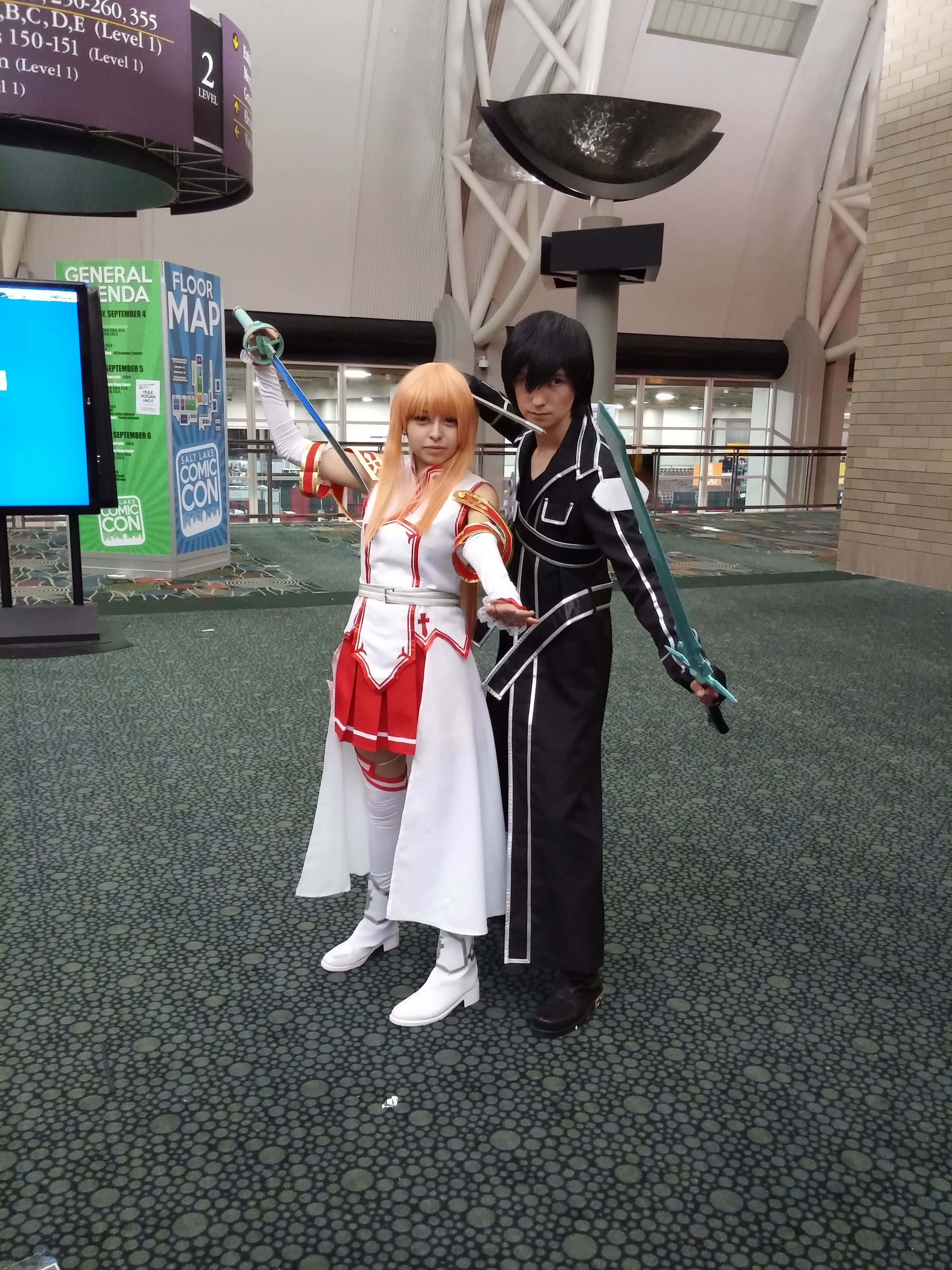 Sword Art Online Cosplay 桌布 壁紙 — 兩位身穿精緻動漫服裝的角色扮演者在會議中心大廳持劍擺姿勢。