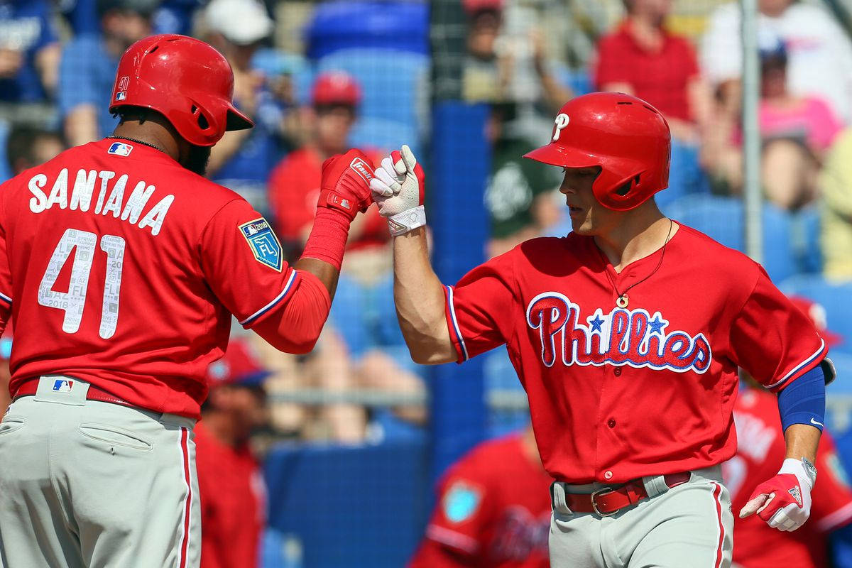 Phillies 桌布 壁紙 — 兩位身穿紅色球衣的費城費城人棒球選手在陽光明媚的日間比賽中擊掌，背景有球迷。