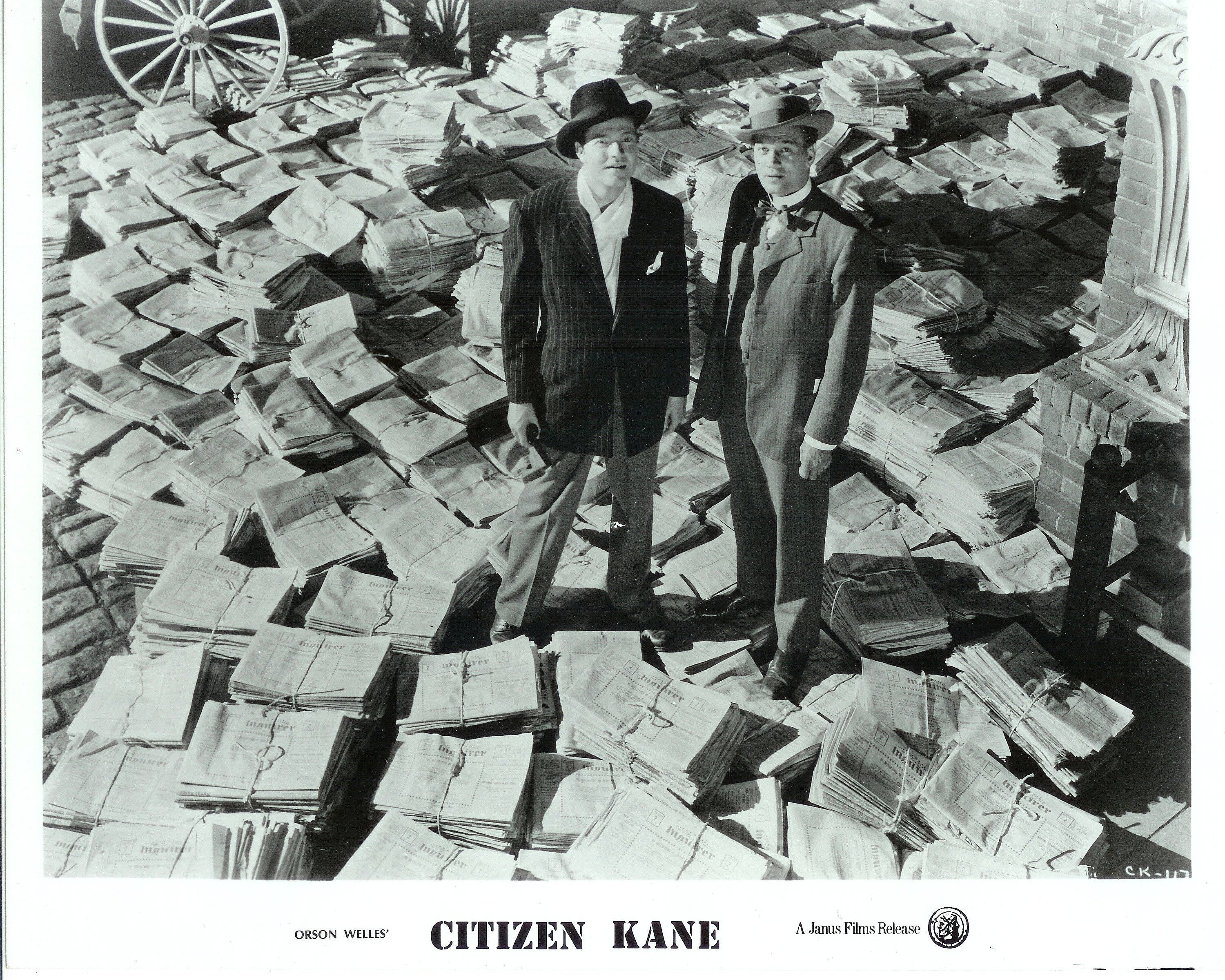 Citizen Kane 桌布 壁紙 — 兩位身穿西裝戴帽子的男士，站在一片報紙堆中，是一張鮮明的黑白電影劇照。