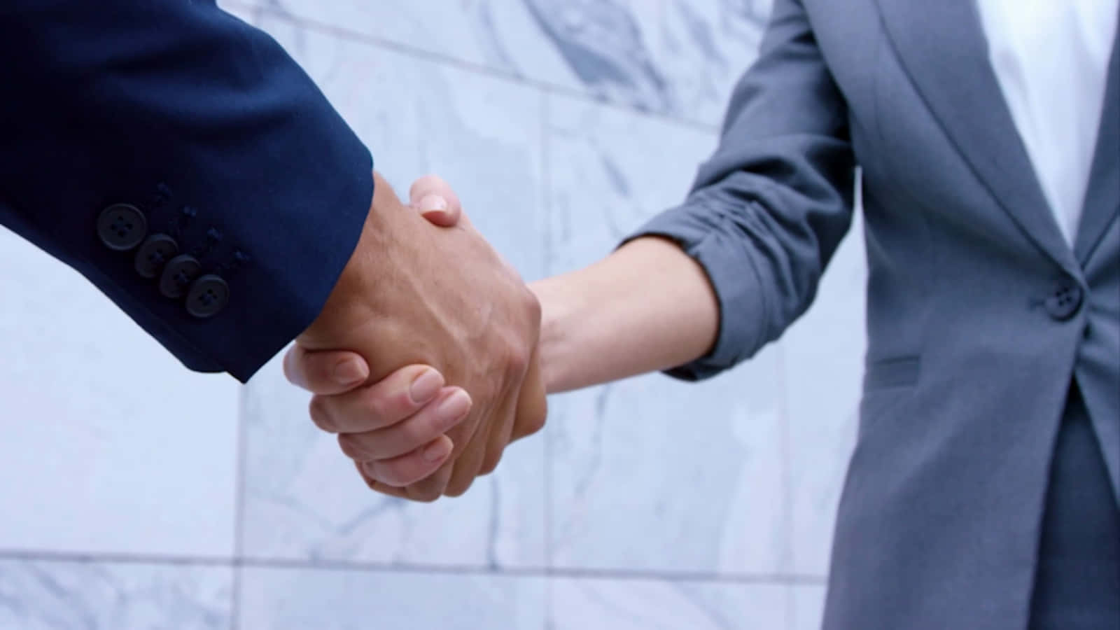 Partnership 桌布 壁紙 — 兩位身穿西裝的商業專業人士在大理石牆背景下堅定地握手。