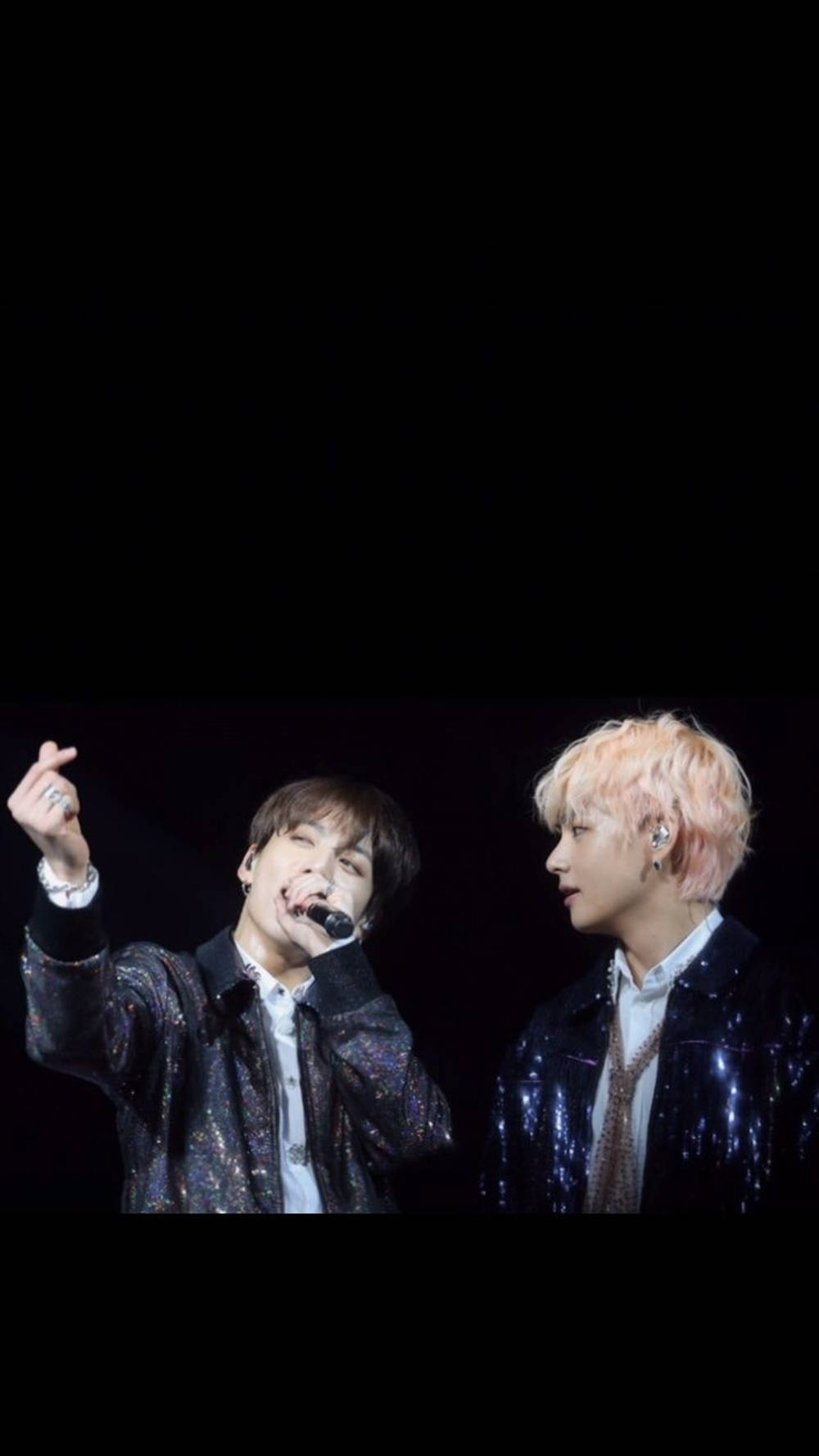 BTS 桌布 壁紙 — 兩位身穿閃亮外套的男表演者在黑色背景的舞台燈光下對著麥克風唱歌。
