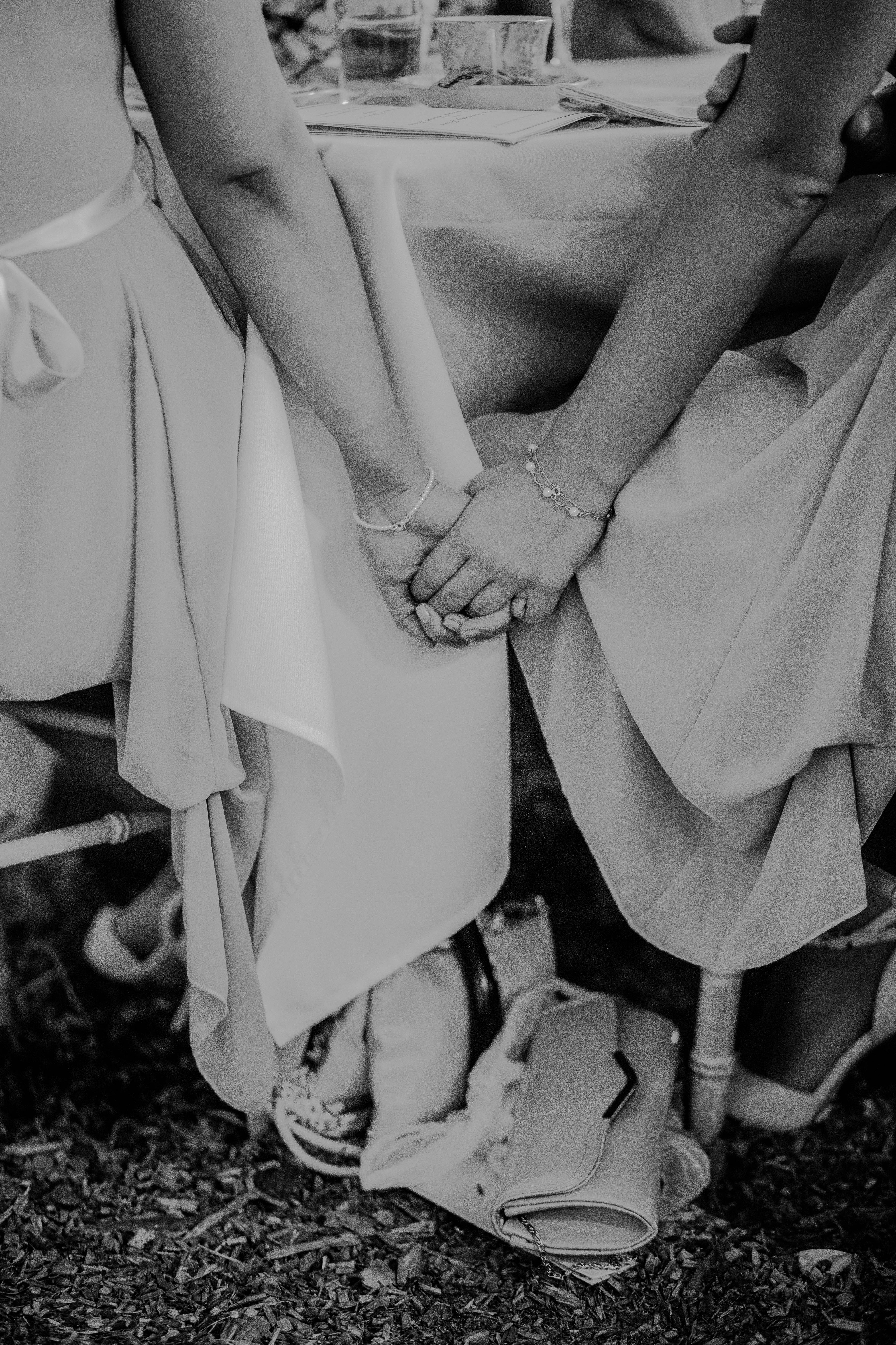 Bridesmaids 桌布 壁紙 — 兩位身穿飄逸長裙的伴娘在黑白婚禮桌上緊緊握著手。