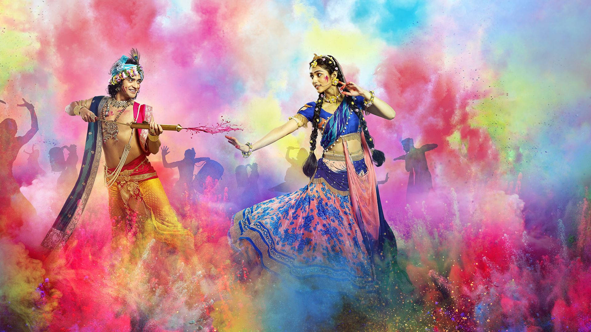 radha krishna serial 桌布 壁紙 — 兩位身穿鮮豔傳統服飾的舞者在胡里節期間，於旋轉的彩虹霧中歡快地拋灑彩色粉末。