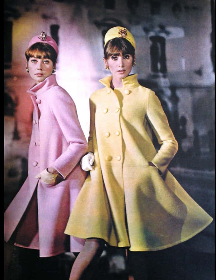 洋裝 桌布 壁紙 — 兩位身穿鮮豔粉紅色和黃色1960年代外套的女性，在模糊的城市背景下自信地擺姿勢。