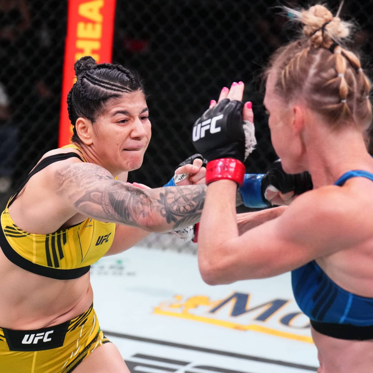 MMA 桌布 壁紙 — 兩位身穿黃色和藍色裝備的女性UFC拳手在八角籠內擊掌，帶有刺青和專注的表情。