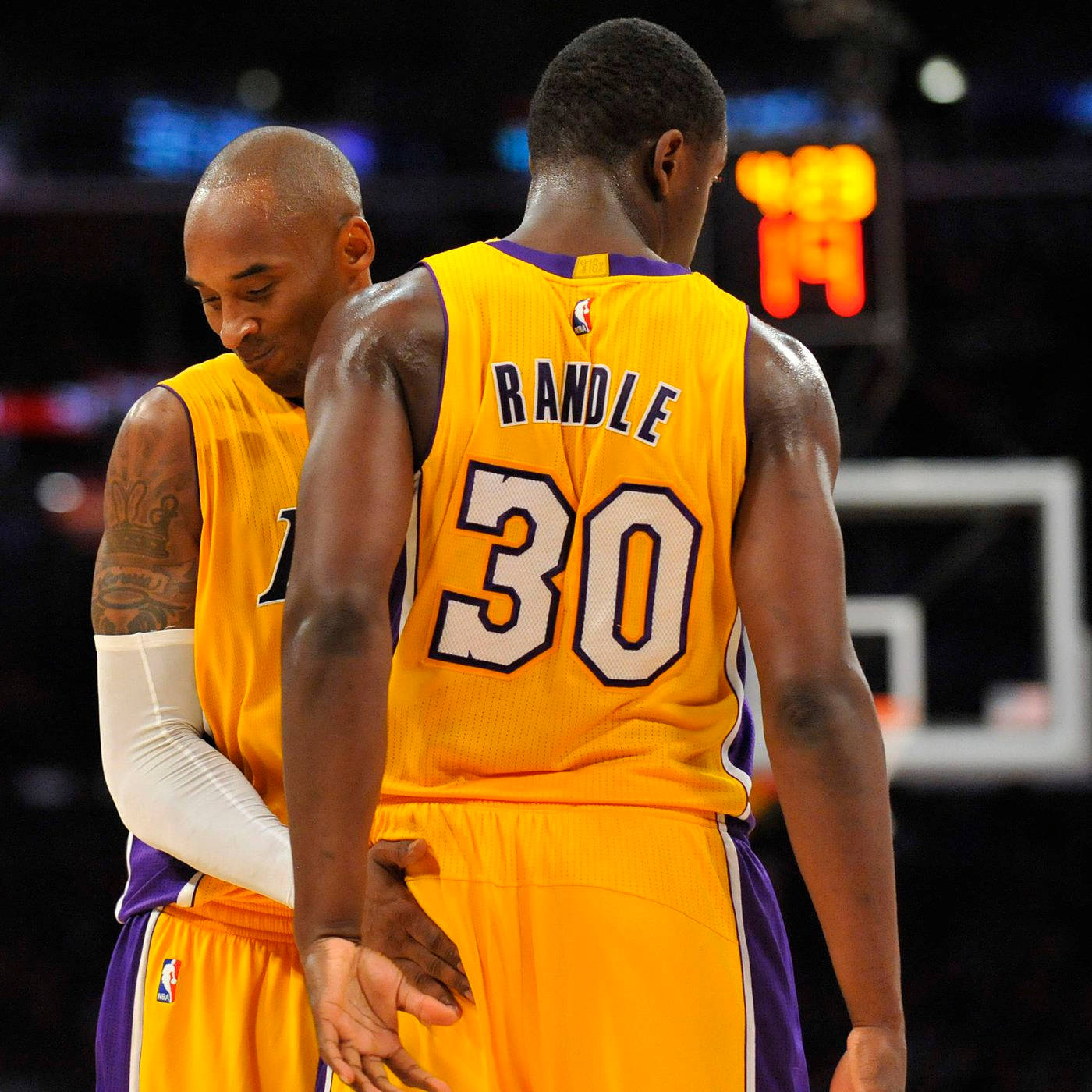 NBA 桌布 壁紙 — 兩位身穿黃色湖人隊球衣的籃球運動員在燈光明亮的球場上，背景有記分板的光芒，共享寧靜時刻。