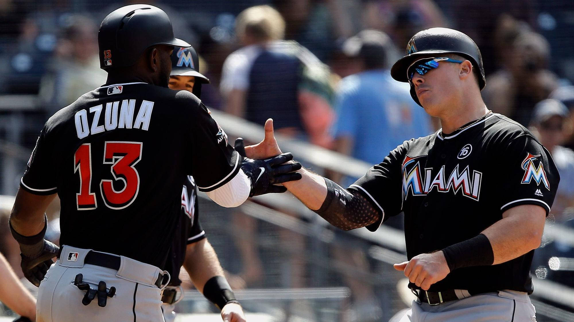 MLB 桌布 壁紙 — 兩位身穿黑色球衣的邁阿密馬林魚棒球選手在陽光明媚的日間比賽中擊掌，背景有模糊的觀眾。