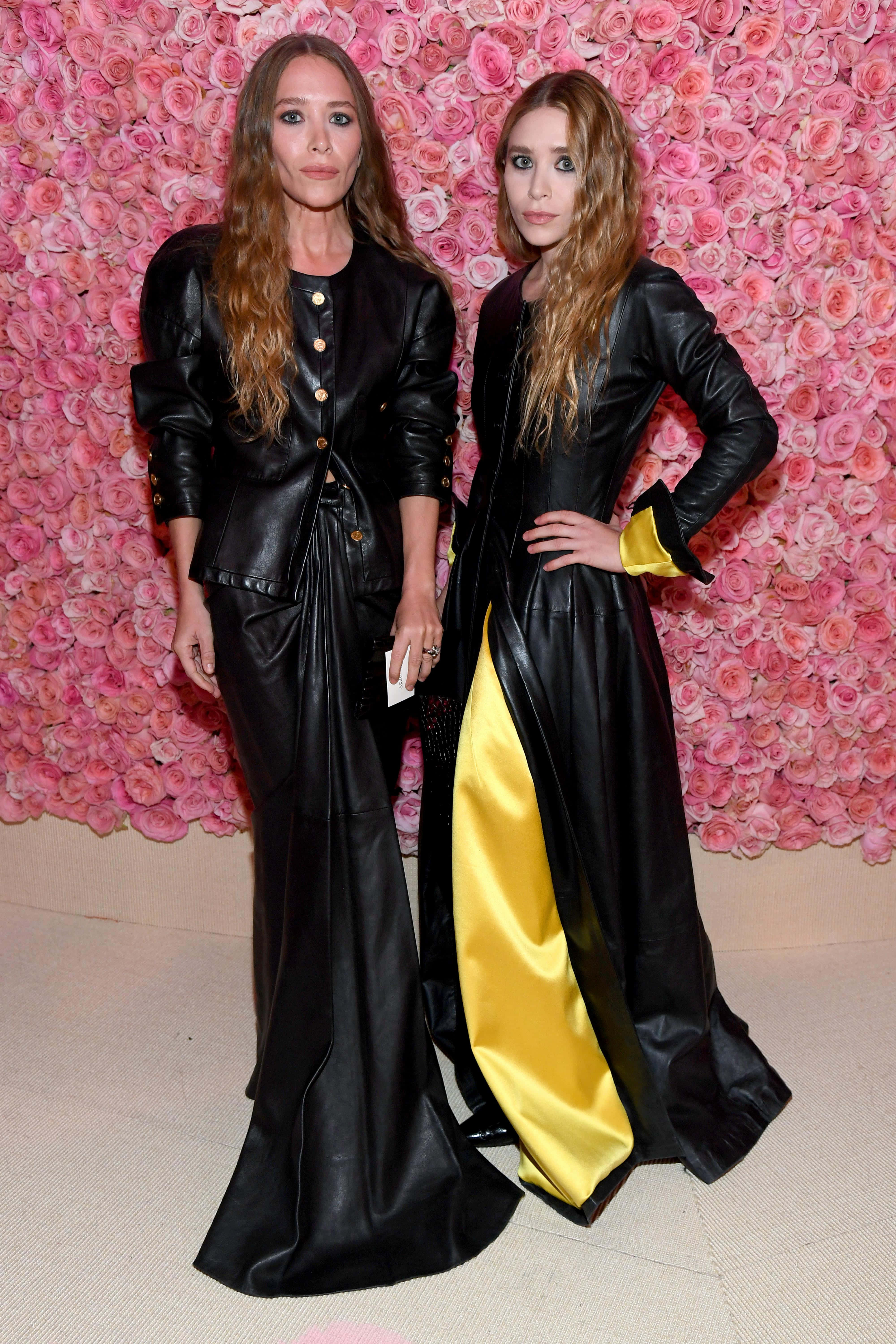 ashley olsen 桌布 壁紙 — 兩位身穿黑色皮革服裝的女性在充滿活力的粉紅玫瑰牆前自信地擺姿勢。