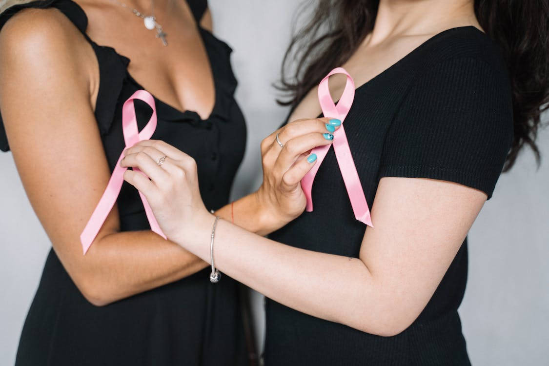 Breast Cancer Awareness 桌布 壁紙 — 兩位身穿黑色連衣裙的女性在純灰色背景前手持粉紅色乳癌意識絲帶。