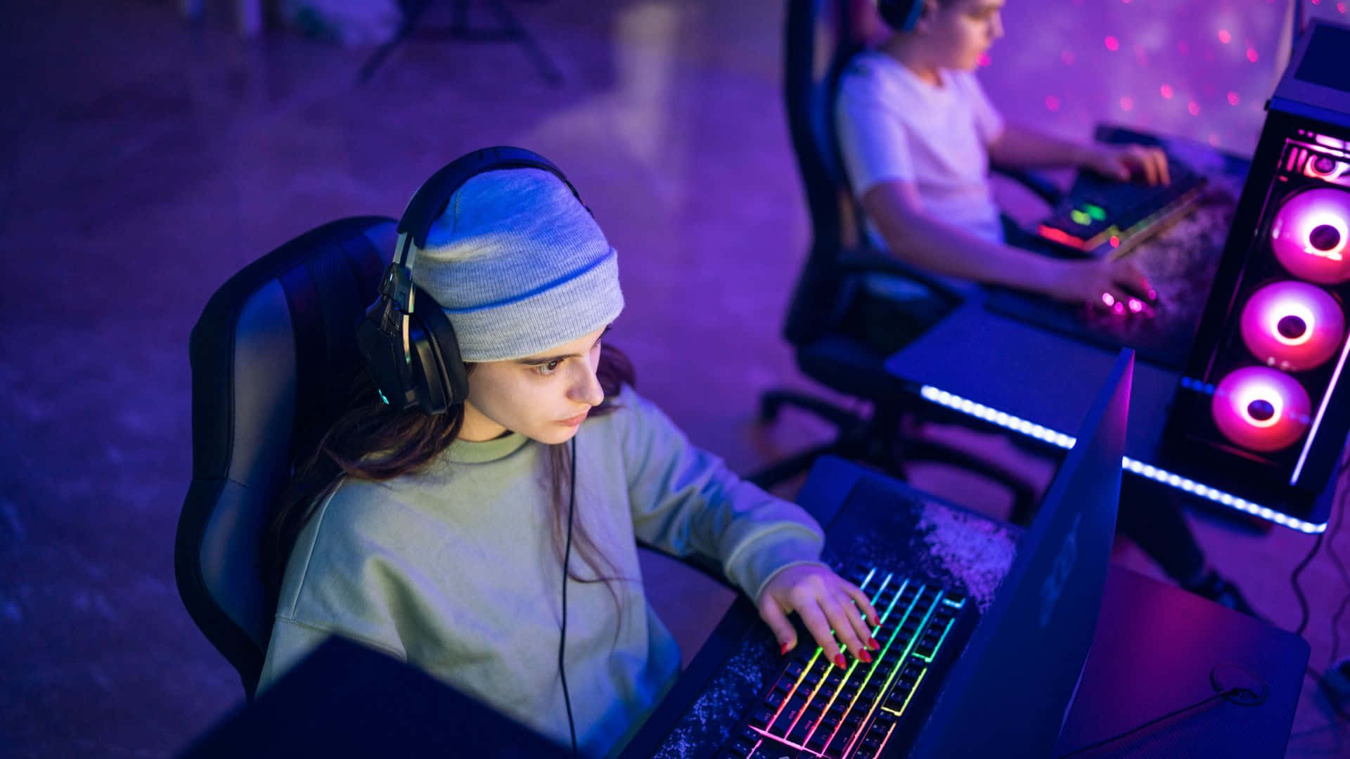 Gaming Tournaments 桌布 壁紙 — 兩位遊戲玩家在昏暗的房間中，被紫色和粉紅色的霓虹燈光包圍，專注於發光的筆記型電腦。