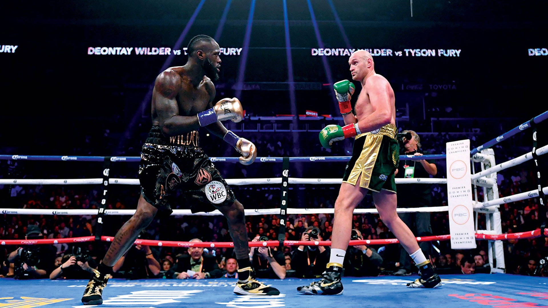 fury 桌布 壁紙 — 兩位重量級拳擊手 Deontay Wilder 和 Tyson Fury 在燈光明亮的擂台上對峙，觀眾歡呼聲震天，頭頂燈光閃爍。