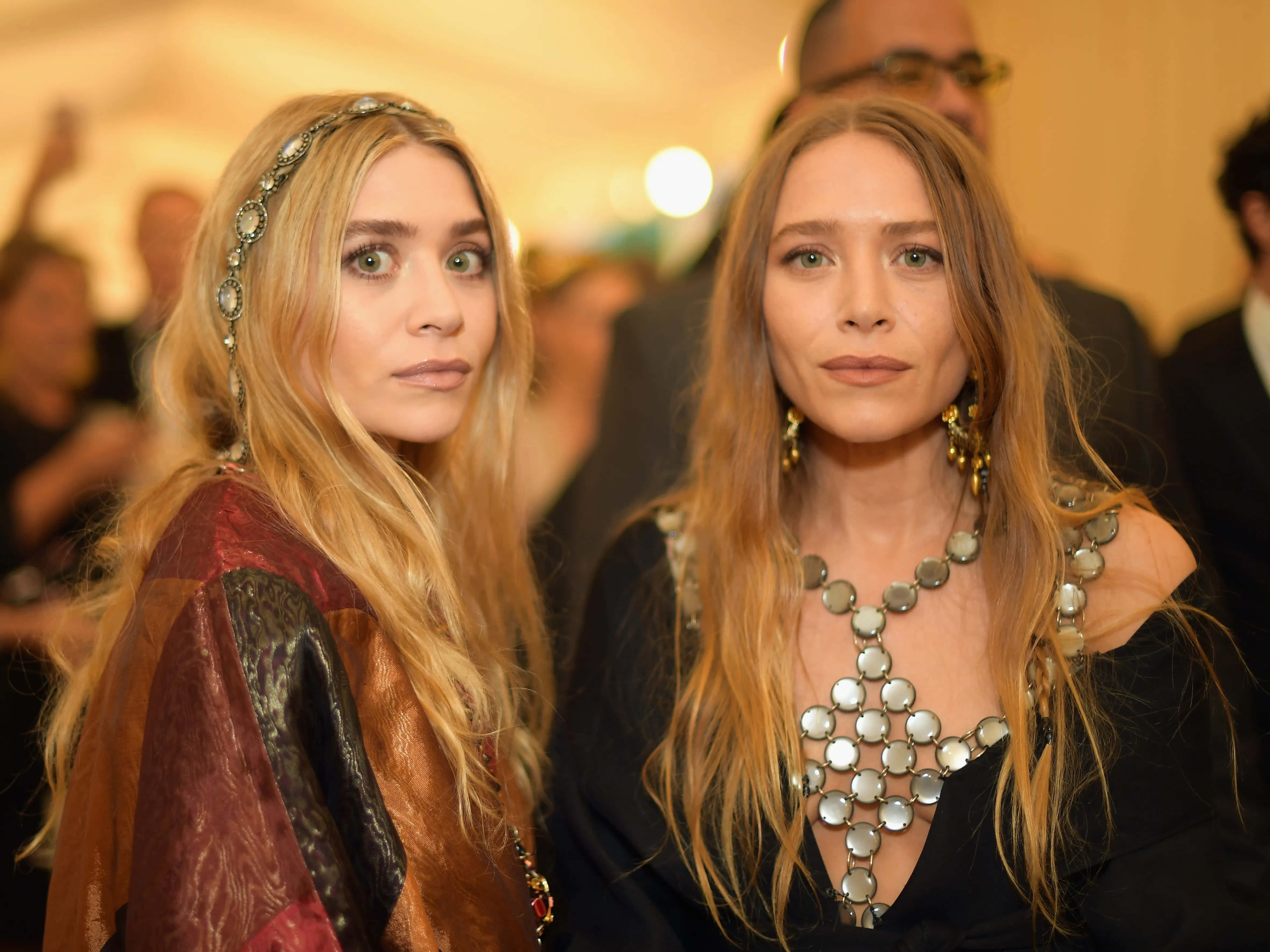ashley olsen 桌布 壁紙 — 兩位長金髮女性在溫暖燈光的室內活動中佩戴華麗珠寶和圖案服裝。