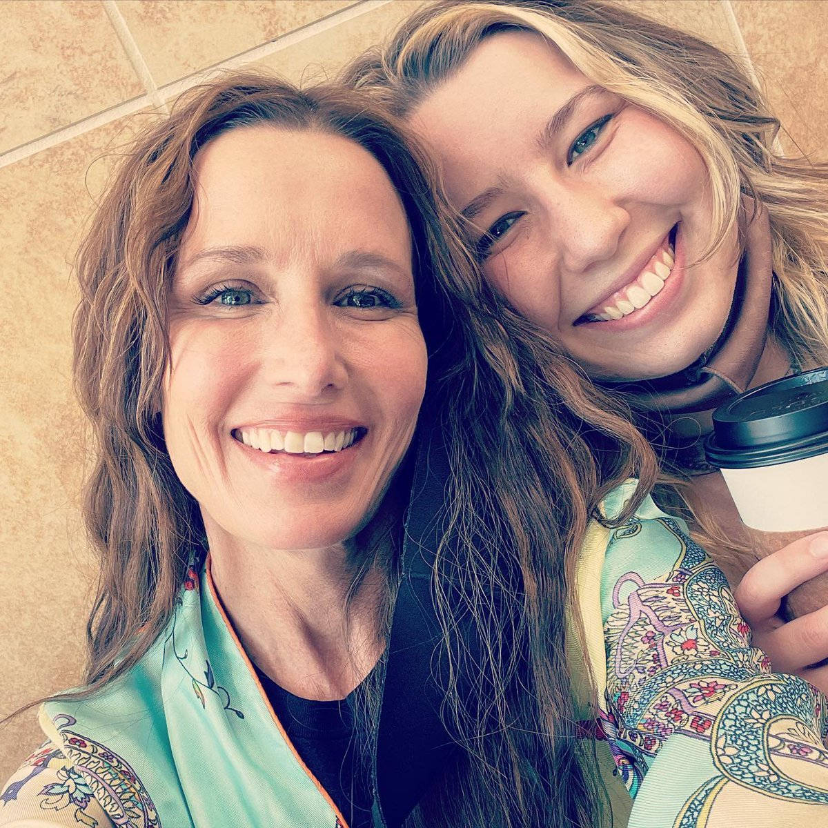 Celebrity 桌布 壁紙 — 兩位長髮微笑的女性在磁磚牆前緊密擁抱，其中一人手持咖啡杯。