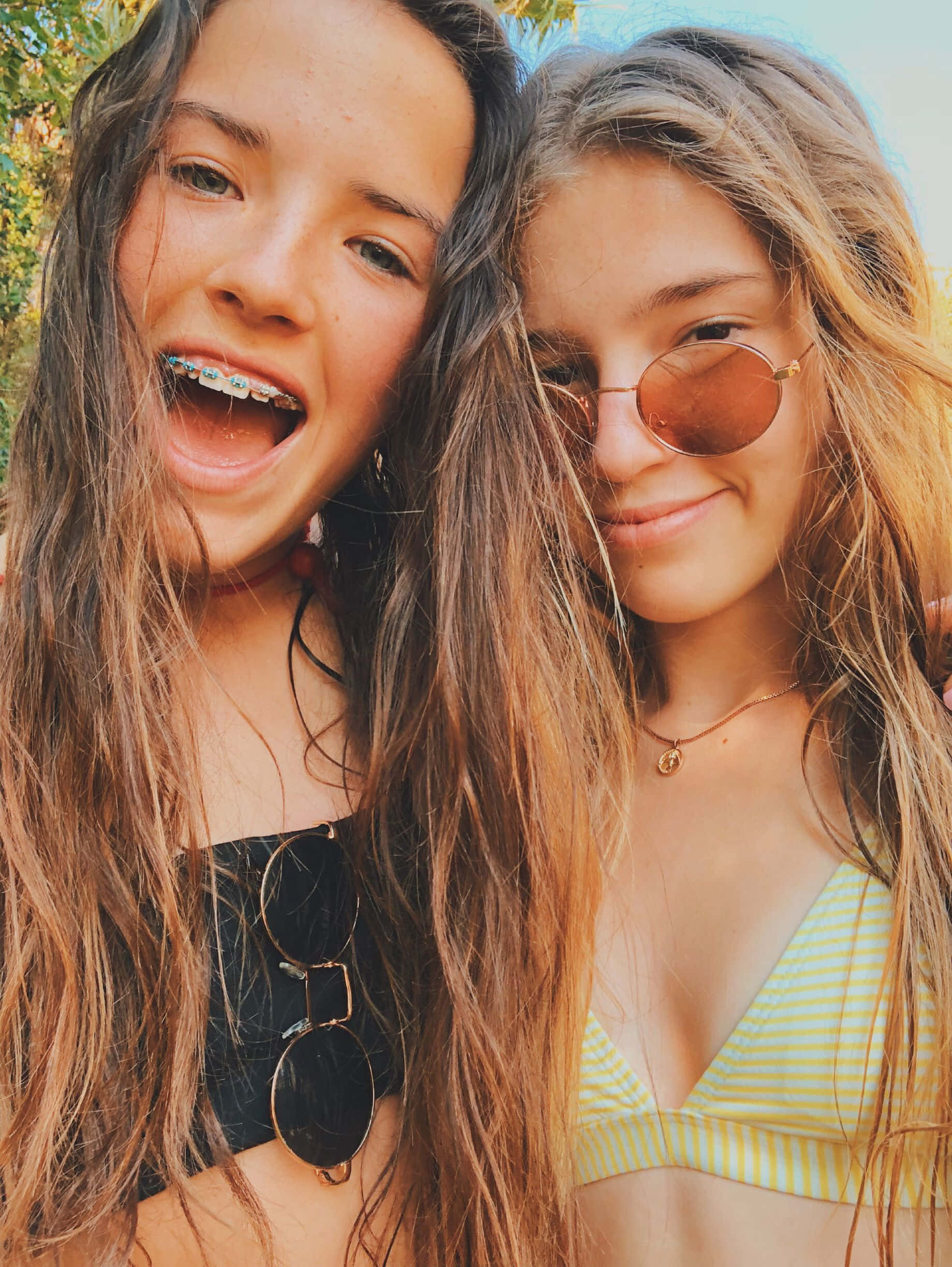 Teenage Girl 桌布 壁紙 — 兩位長髮微笑的年輕女性，一位戴著牙套和太陽眼鏡，另一位穿著條紋比基尼上衣在戶外。