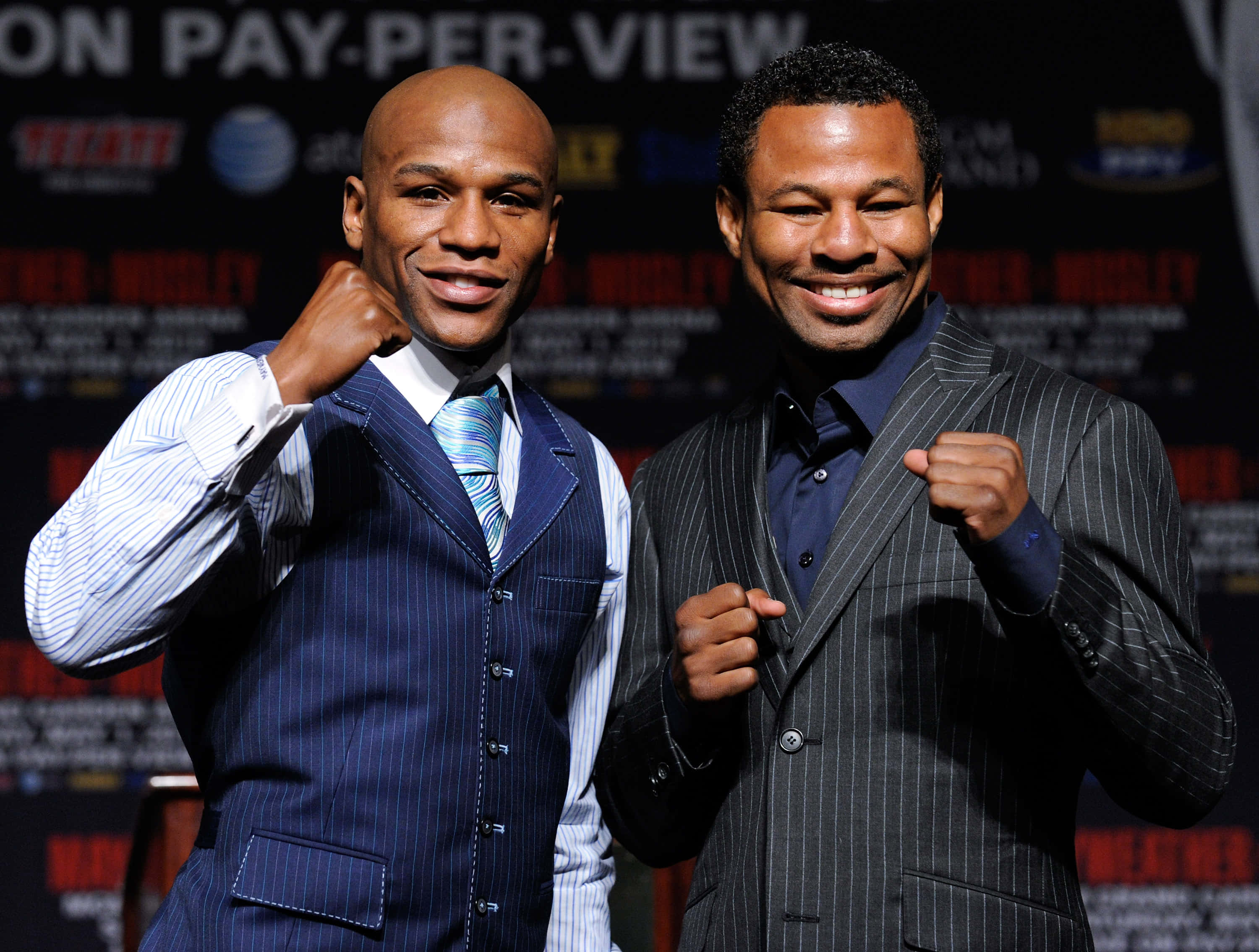 Boxing 桌布 壁紙 — 兩位面帶微笑的拳擊手身穿細條紋西裝，在品牌背景前的新聞活動中舉起拳頭擺姿勢。