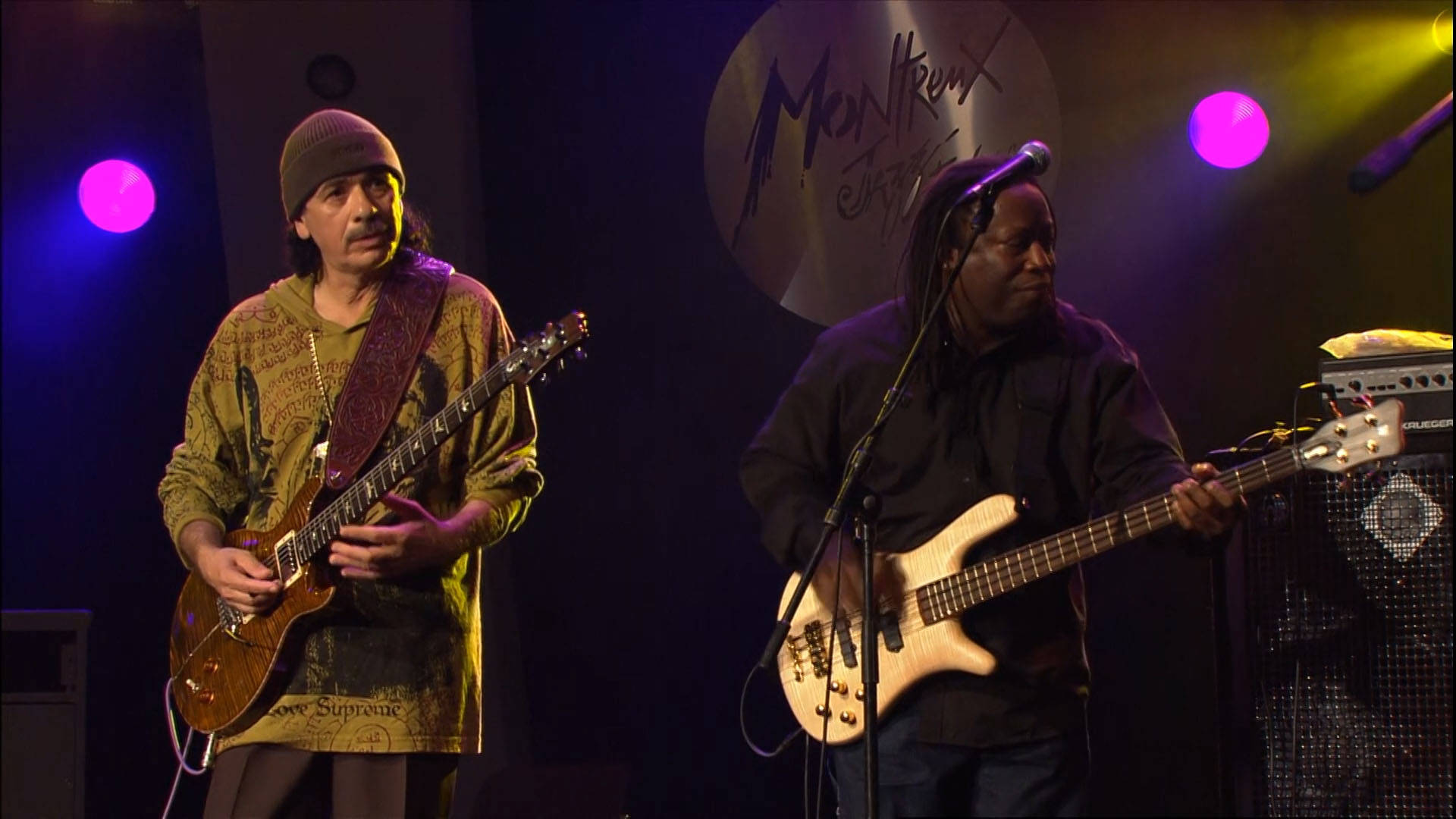音樂 桌布 壁紙 — 兩位音樂家在彩色聚光燈下在舞台上表演，背後有 Montreux Jazz 標誌。