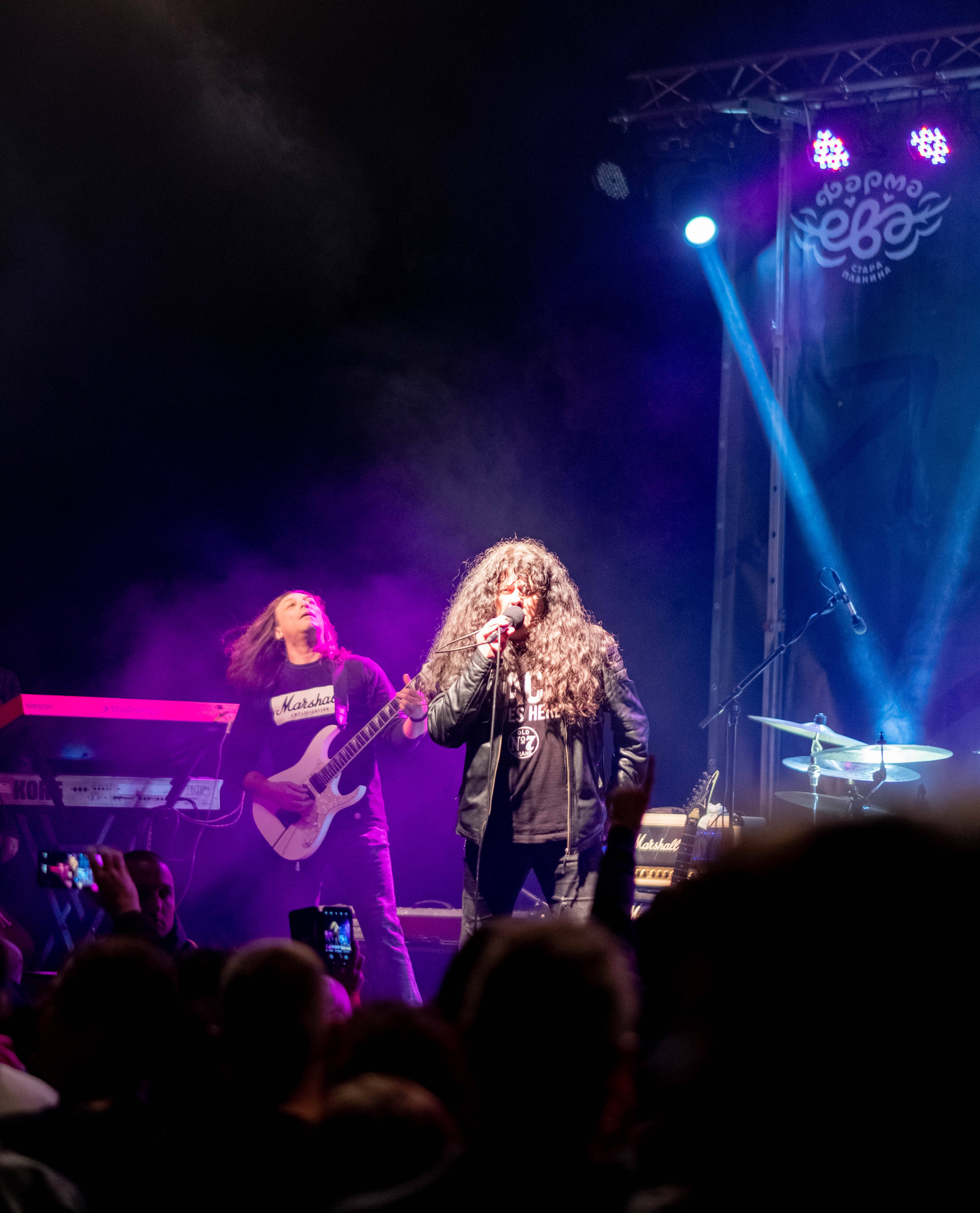 Serbia 桌布 壁紙 — 兩位音樂家在煙霧瀰漫的舞台上表演，舞台沐浴在紫色和藍色的燈光中，前景是投入的觀眾。