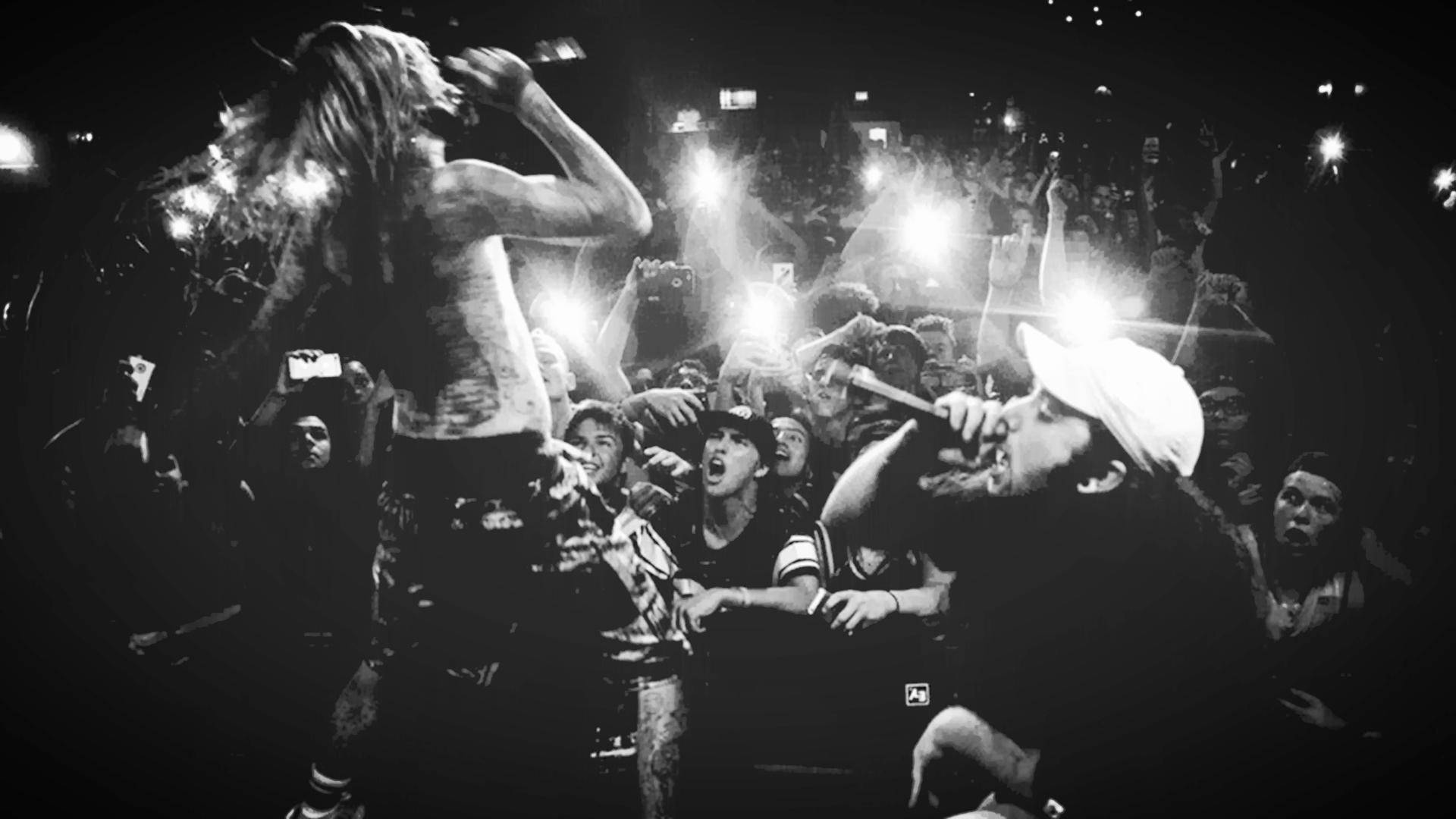 suicideboys 桌布 壁紙 — 兩位音樂家在舞台上充滿活力地表演，一群粉絲在黑暗的音樂會場地中舉起發光的手機。