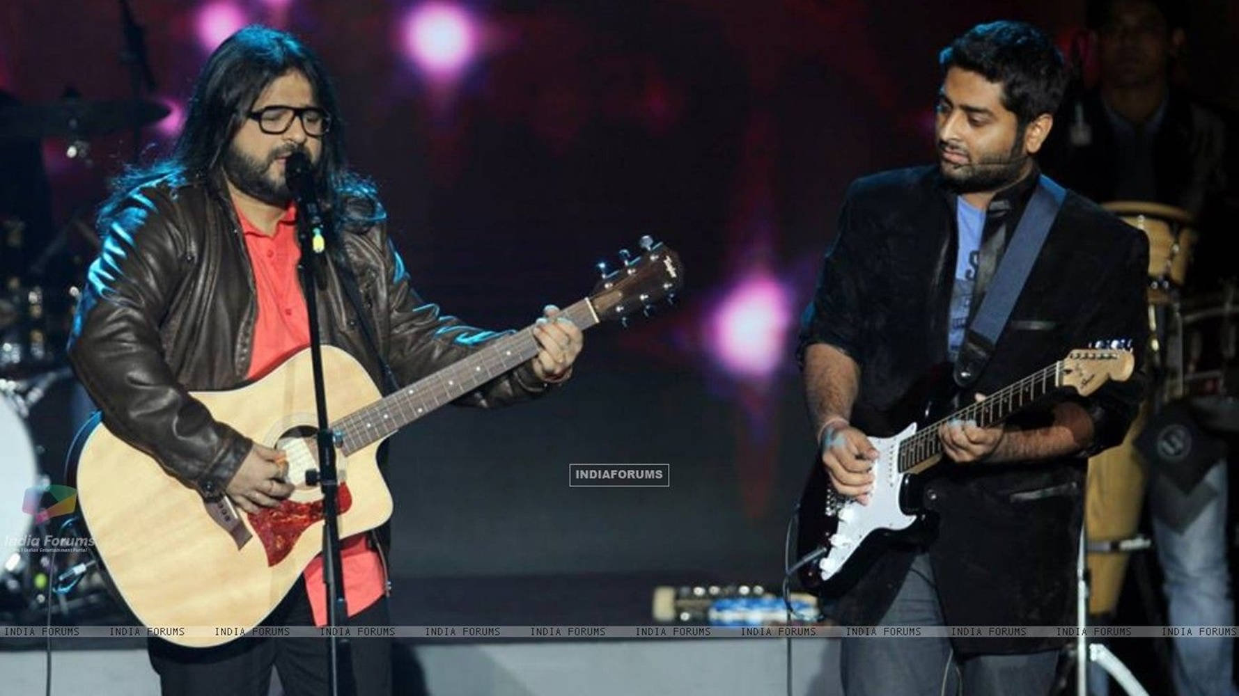 Indian 桌布 壁紙 — 兩位音樂家在舞台上現場表演，一位彈奏木吉他，另一位在彩色舞台燈光下彈奏電吉他。