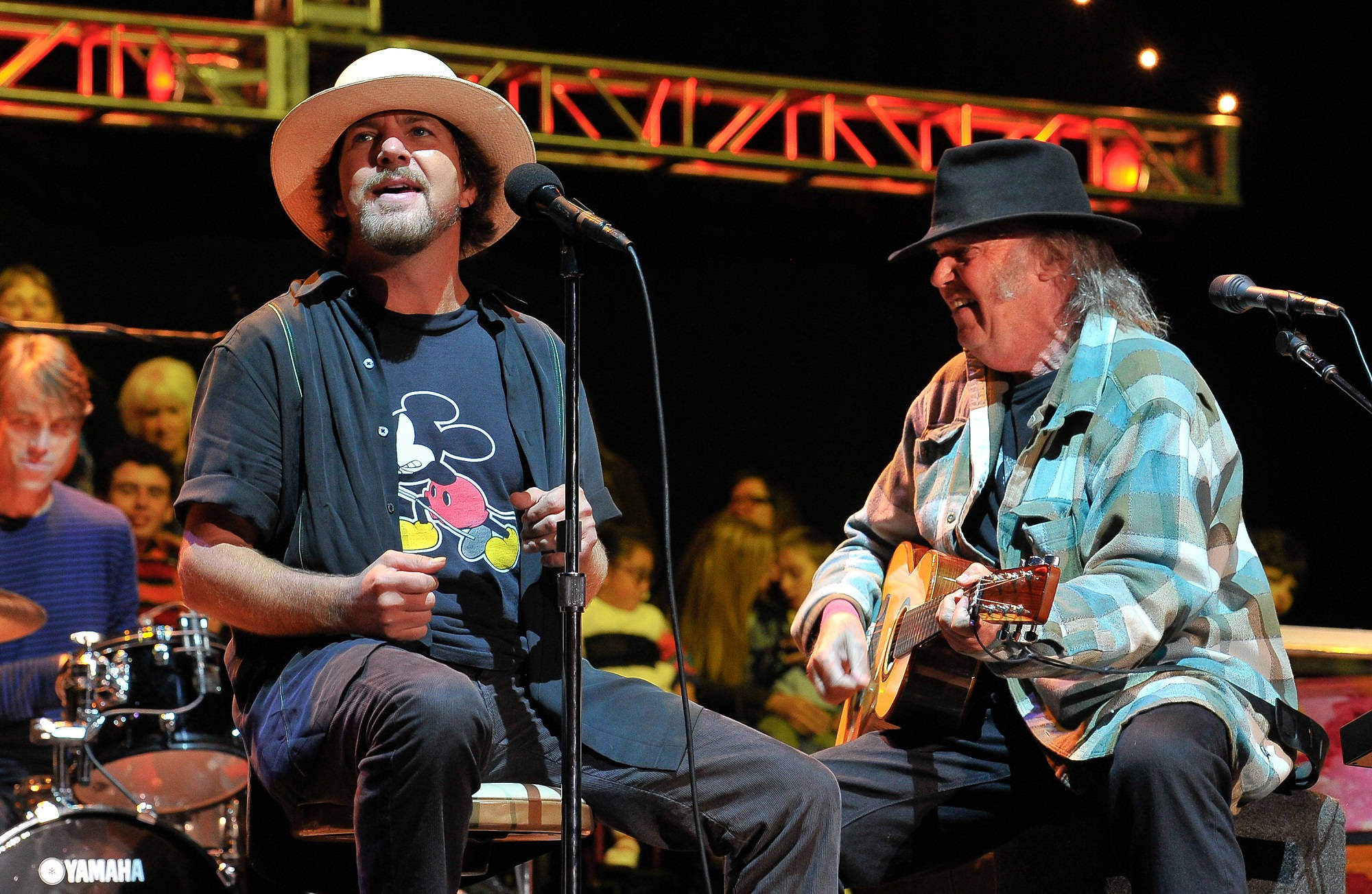 pearl jam 桌布 壁紙 — 兩位音樂家在舞台上現場表演，一位對著麥克風唱歌，另一位在溫暖的舞台燈光下彈奏木吉他。