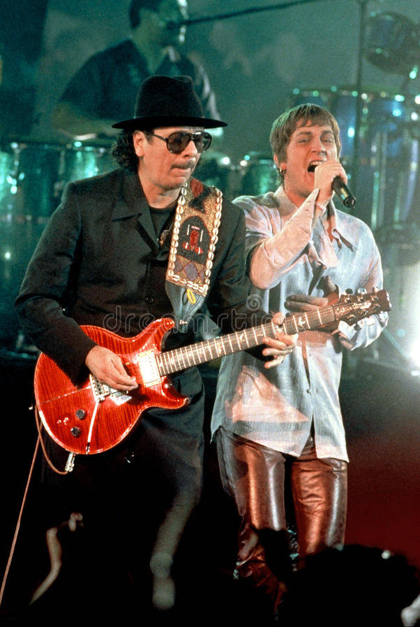guitar player 桌布 壁紙 — 兩位音樂家在舞台上表演，一位彈奏紅色電吉他，另一位在明亮的舞台燈光下對著麥克風唱歌。