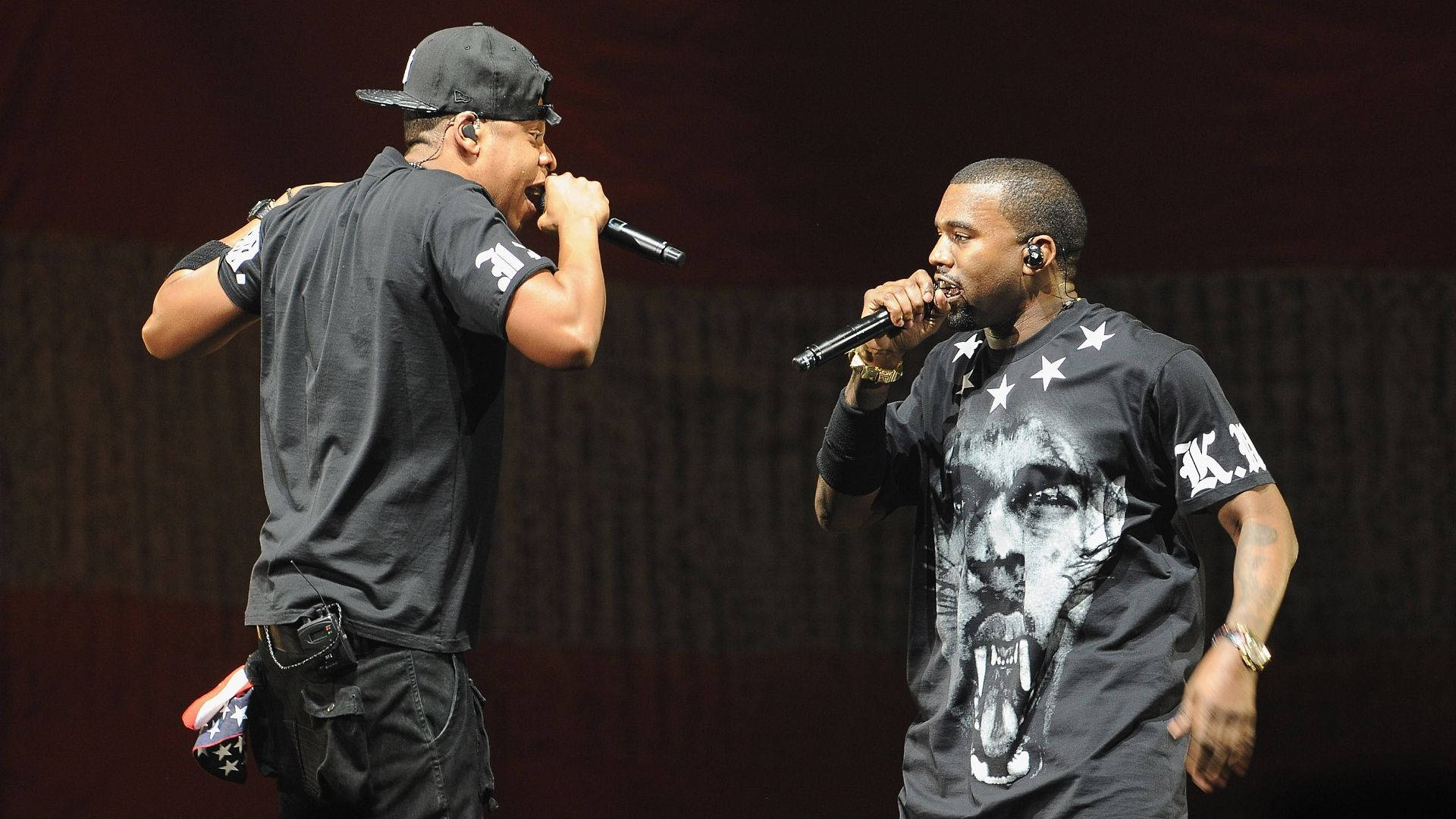 Jay-z 桌布 壁紙 — 兩位饒舌歌手在明亮的舞台燈光下手持麥克風充滿活力地表演。