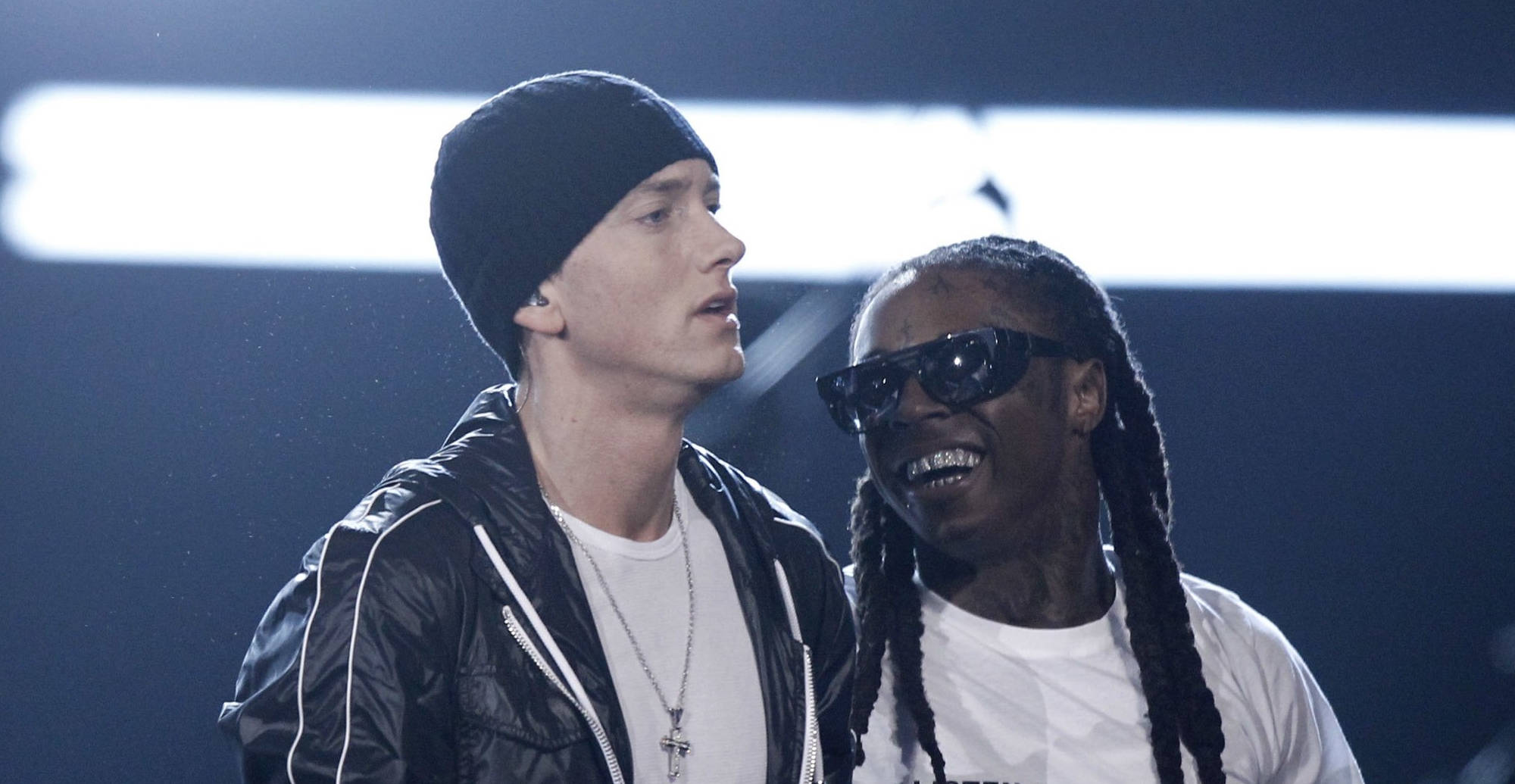 Lil Wayne 桌布 壁紙 — 兩位饒舌歌手在舞台上，一位戴黑色毛帽和外套，另一位戴太陽眼鏡和辮子，兩人在明亮的舞台燈光下微笑。
