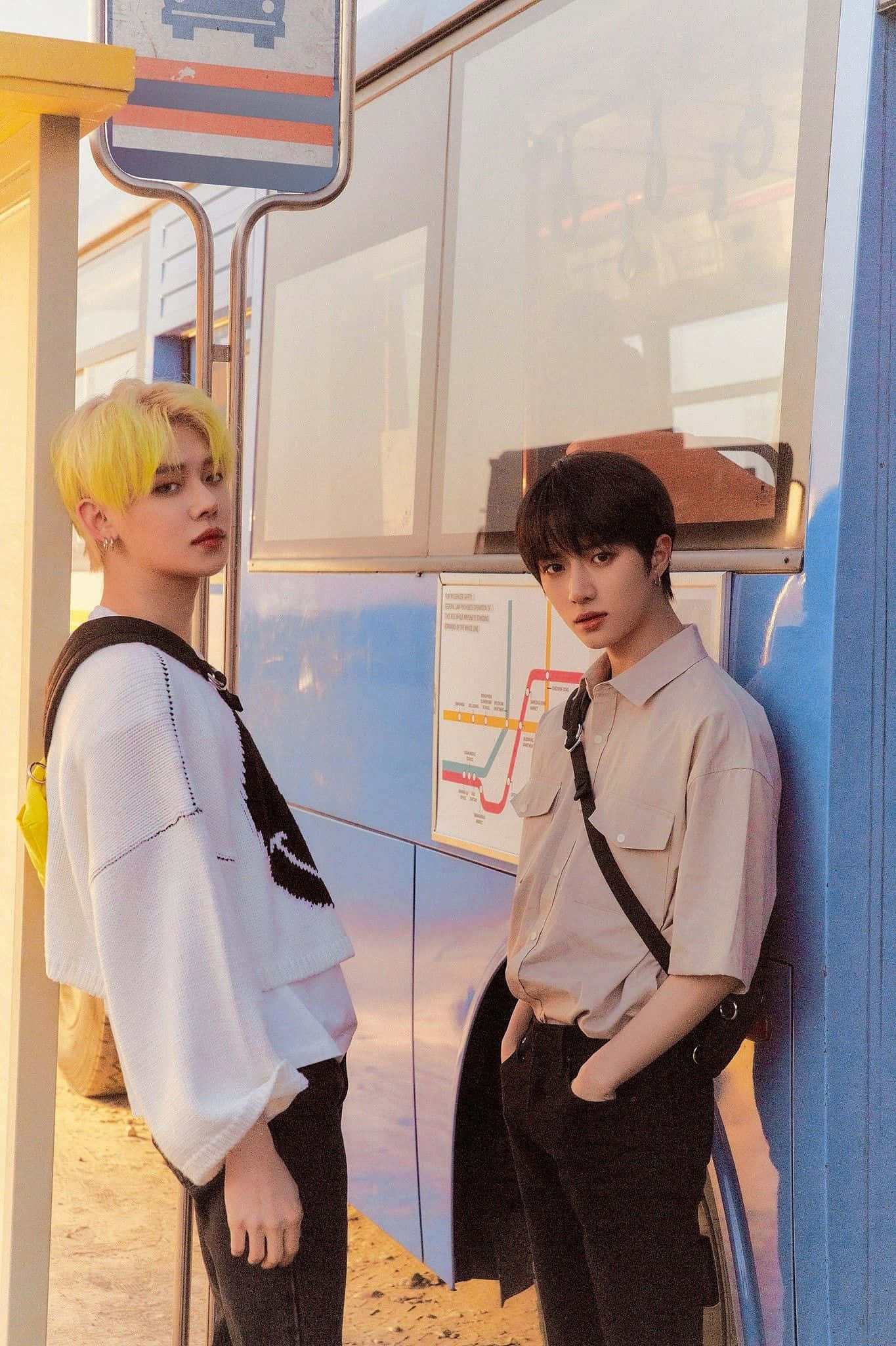 Big Hit Entertainment 桌布 壁紙 — 兩位髮型不同的年輕男子在溫暖的金色光線下站在色彩繽紛的公車站。