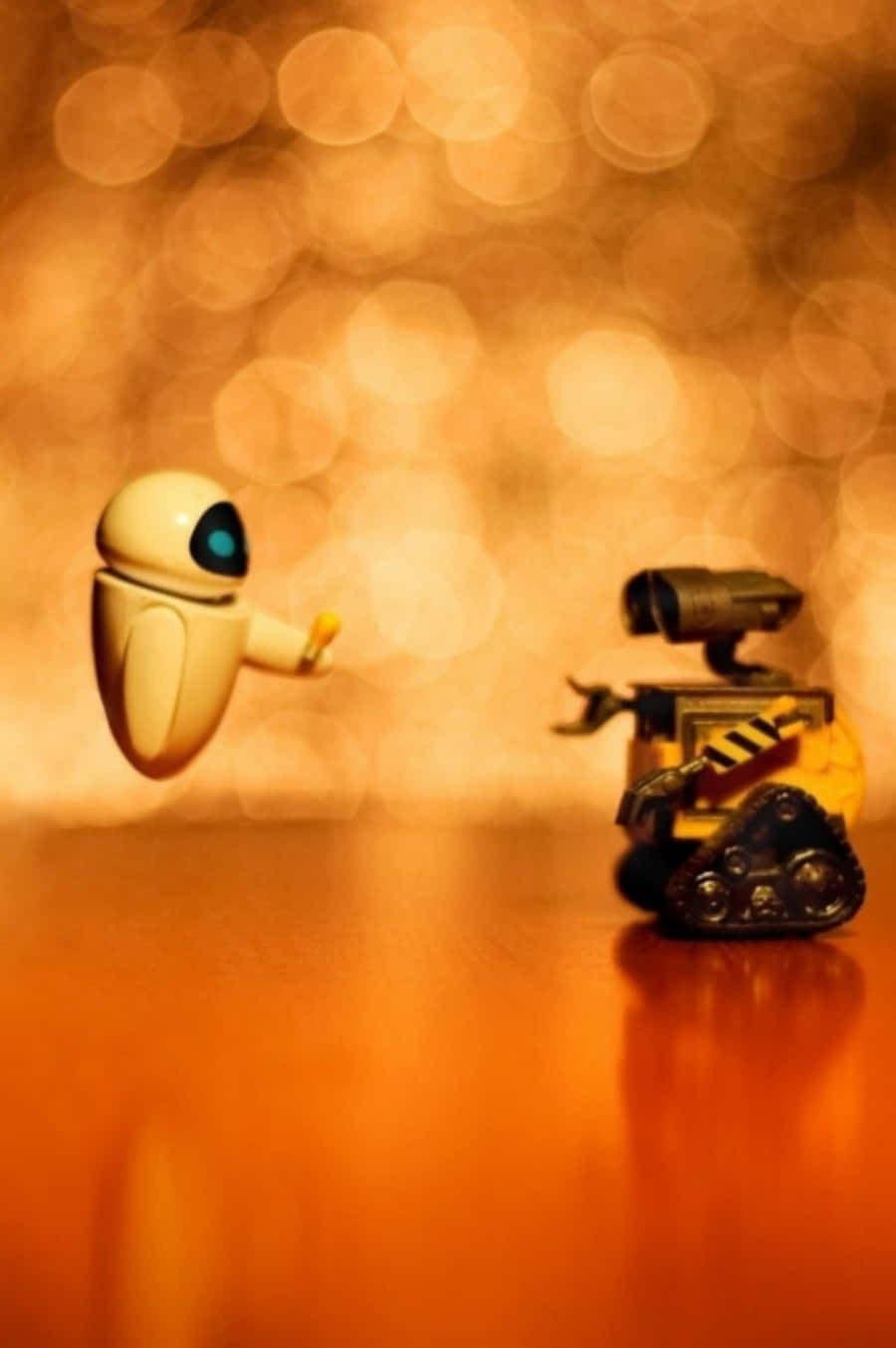 瓦力 桌布 壁紙 — 兩個 Pixar 機器人在溫暖的木質表面上漂浮和站立，背景是發光的金色散景。