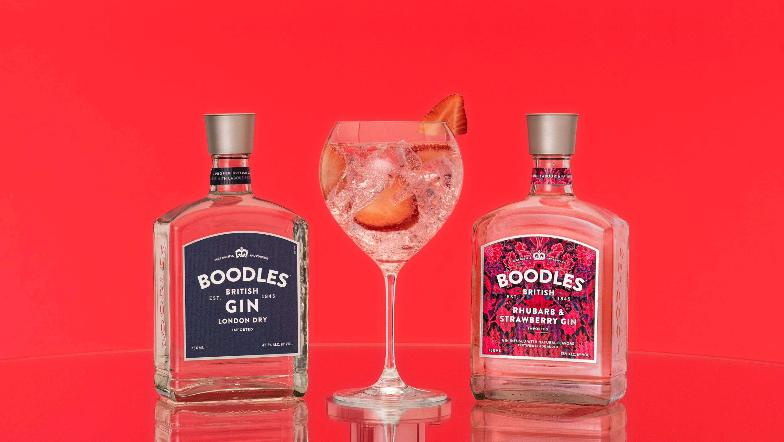 cocktail 桌布 壁紙 — 兩個Boodles琴酒瓶夾著一個裝滿冰塊和水果的琴酒雞尾酒杯，放在光滑的紅色表面上。