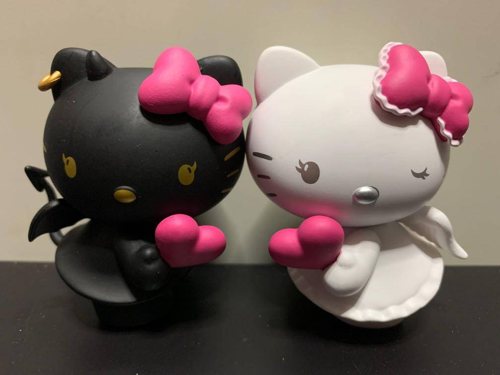 Hello Kitty Halloween 桌布 壁紙 — 兩個Hello Kitty公仔，一個黑色惡魔，一個白色天使，都在純色背景前拿著粉紅色愛心。