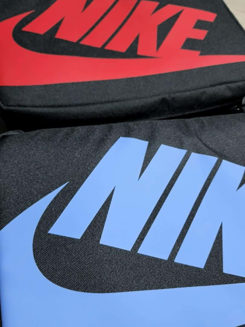 Shoe Box 桌布 壁紙 — 兩個Nike品牌袋的特寫，一個有紅色標誌，另一個有藍色標誌，兩者都在黑色布料上。