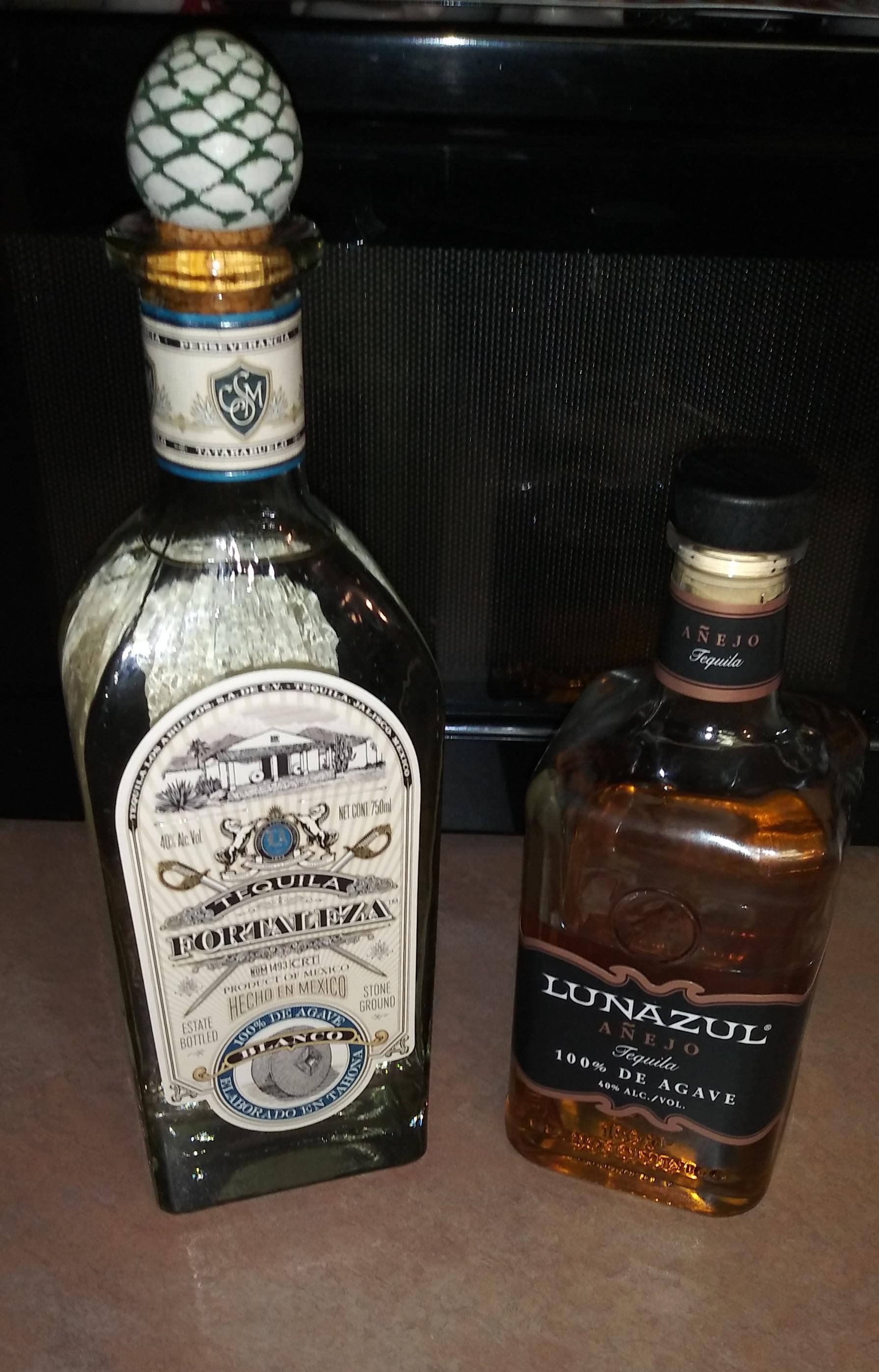 alcohol 桌布 壁紙 — 兩個不同的龍舌蘭酒瓶，一個帶有鳳梨塞和華麗標籤，另一個帶有琥珀色液體和時尚黑色瓶蓋，並排放在檯面上。