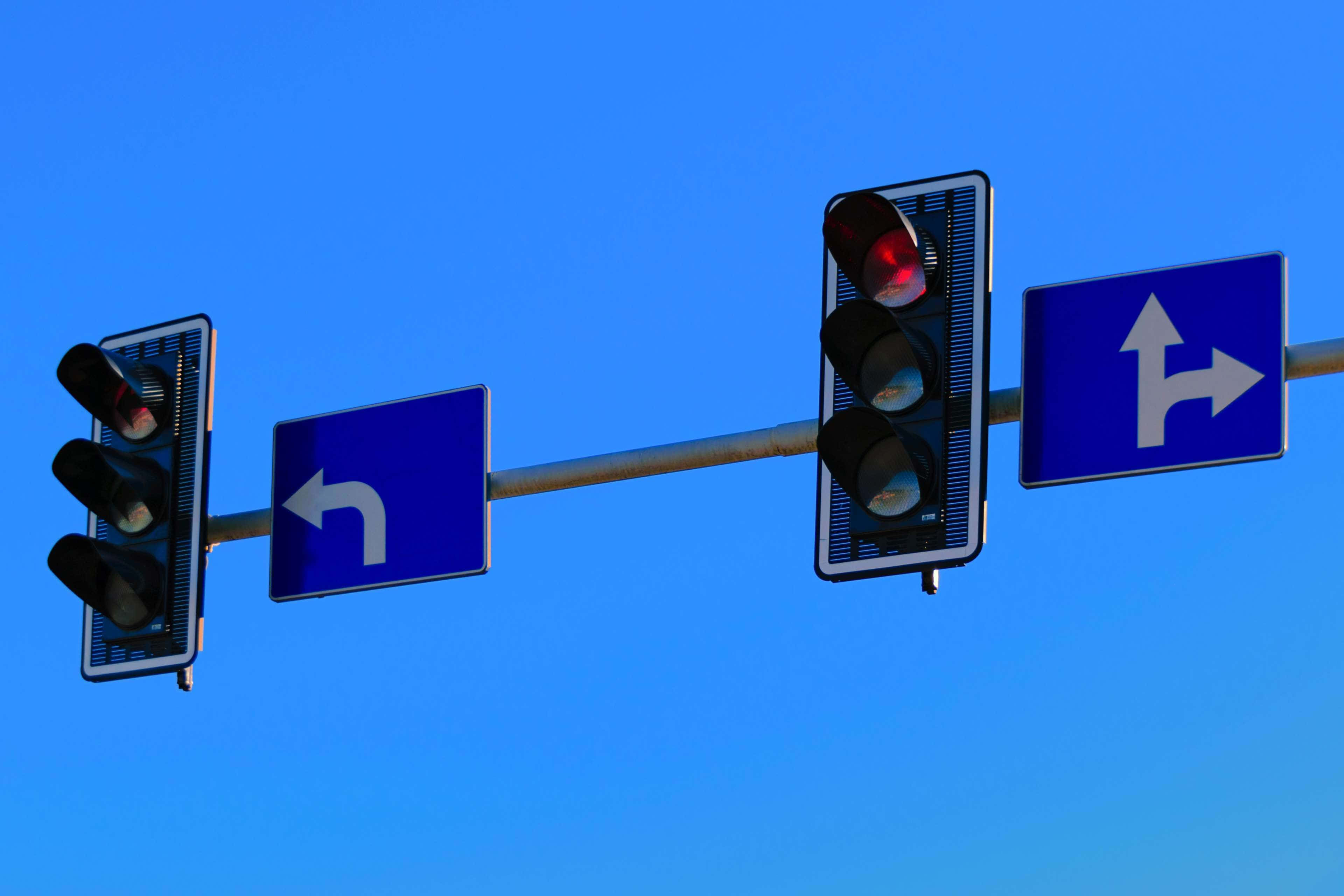 Stop Light 桌布 壁紙 — 兩個交通號誌和方向標誌安裝在柱子上，背景是晴朗的藍天。