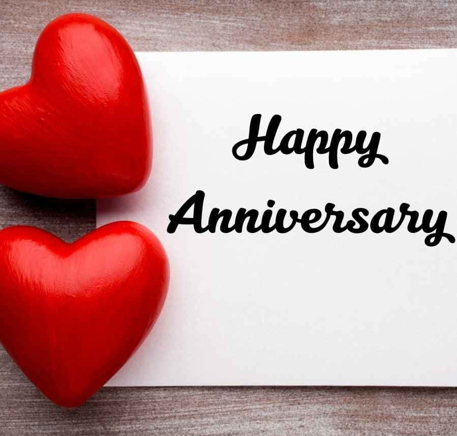 Anniversary 桌布 壁紙 — 兩個亮面紅色心形放在木質表面上，旁邊有一張白色卡片，上面寫著 'Happy Anniversary'。