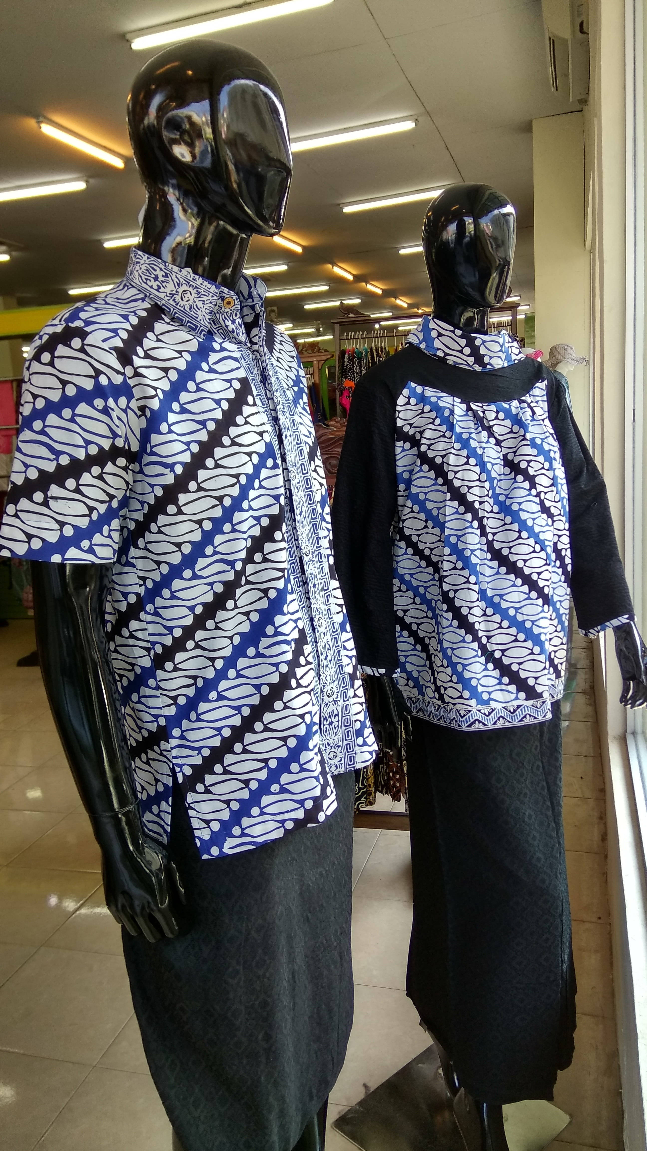 Clothes 桌布 壁紙 — 兩個亮面黑色人體模型在光線充足的零售店展示鮮豔的藍、白、黑色蠟染襯衫。