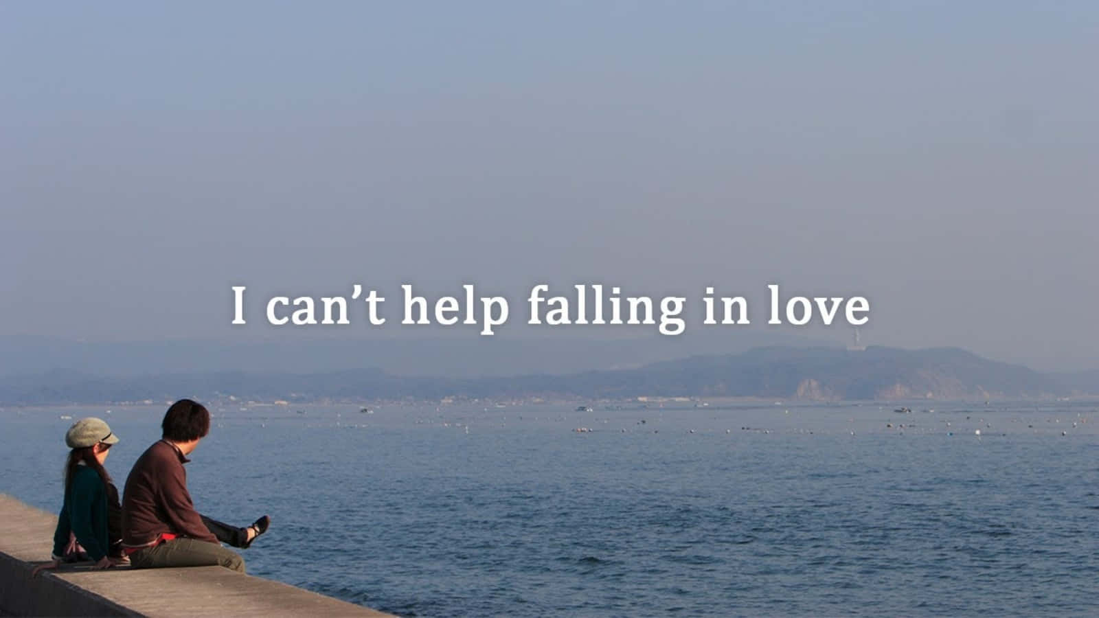 Falling In Love 桌布 壁紙 — 兩個人並排坐在混凝土碼頭上，俯瞰著平靜的藍色大海，遠處有朦朧的山巒，天空柔和。