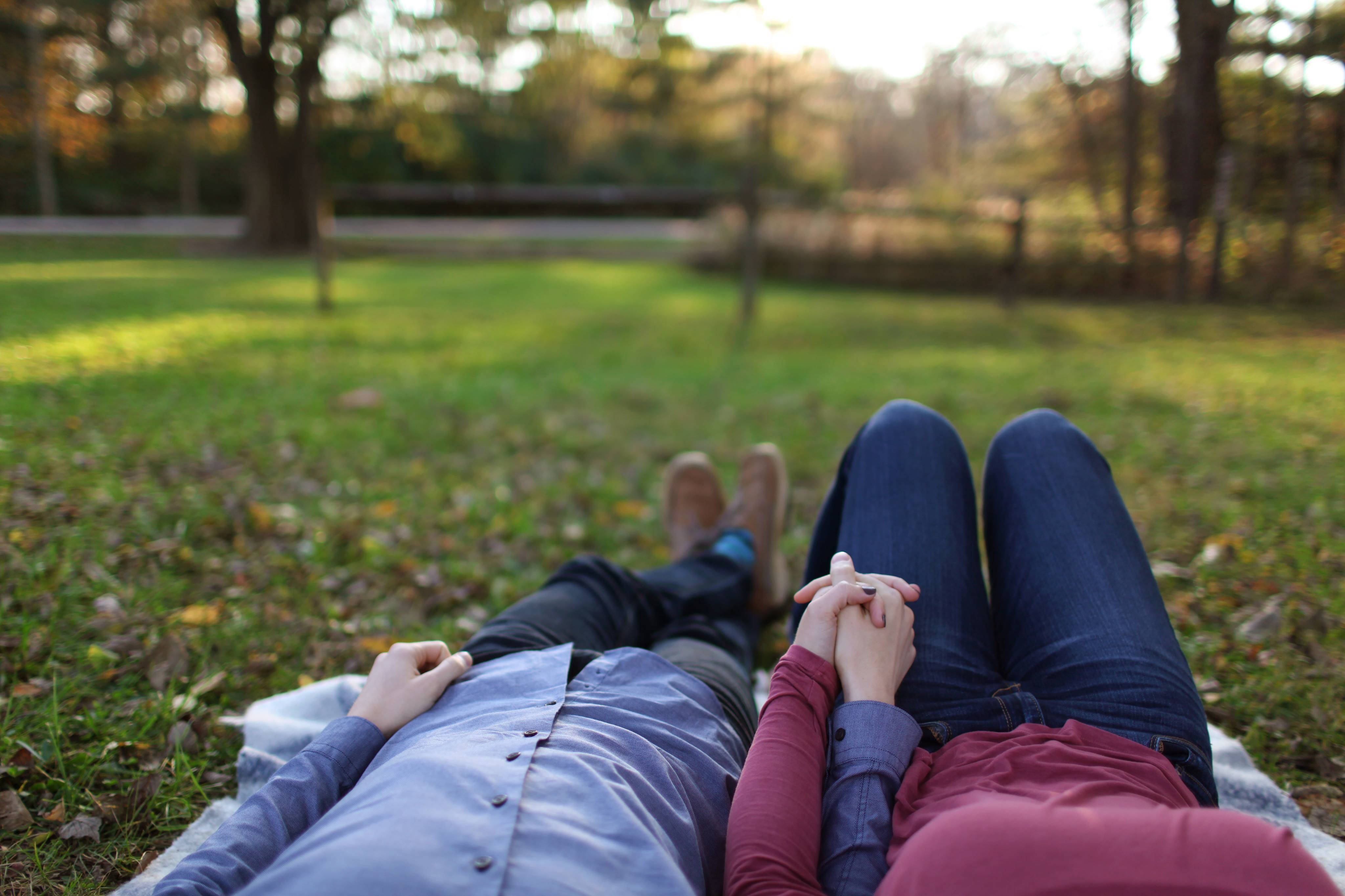 Romantic 桌布 壁紙 — 兩個人並排躺在草地上牽著手，身後秋天的樹木間透出金色的陽光。