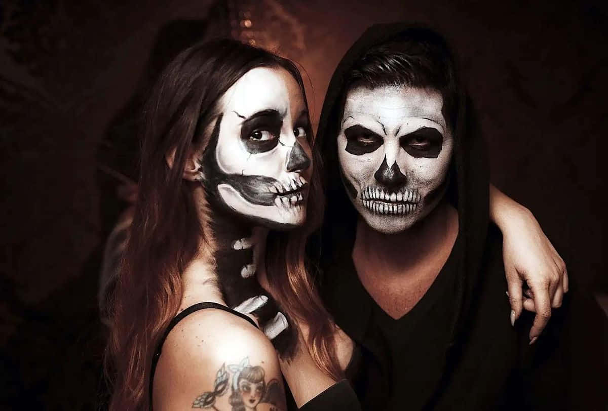 Creepy Halloween 桌布 壁紙 — 兩個人化著精緻的骷髏妝，在昏暗的燈光下緊密地擺姿勢，其中一人穿著連帽衣物。