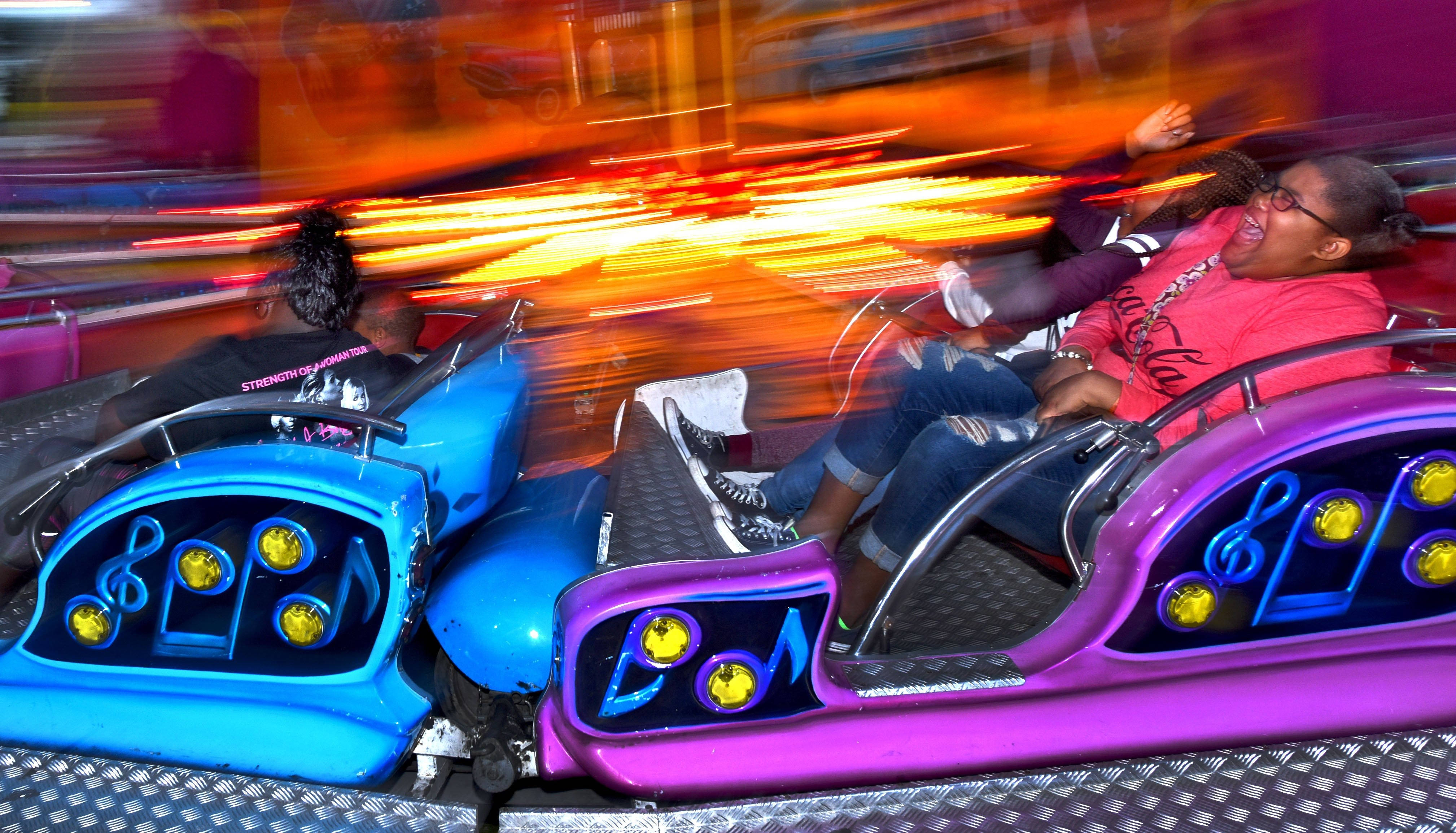 Roller Coaster 桌布 壁紙 — 兩個人在一個旋轉的音樂遊樂設施上歡樂地大笑，周圍有發光的燈光和橙色與藍色的動態模糊條紋。