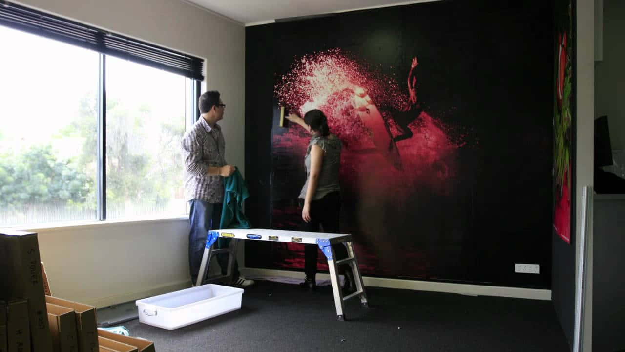 Installation Art 桌布 壁紙 — 兩個人在一個現代房間內安裝一幅充滿活力的紅黑抽象壁紙，其設計帶有動態的潑濺效果。