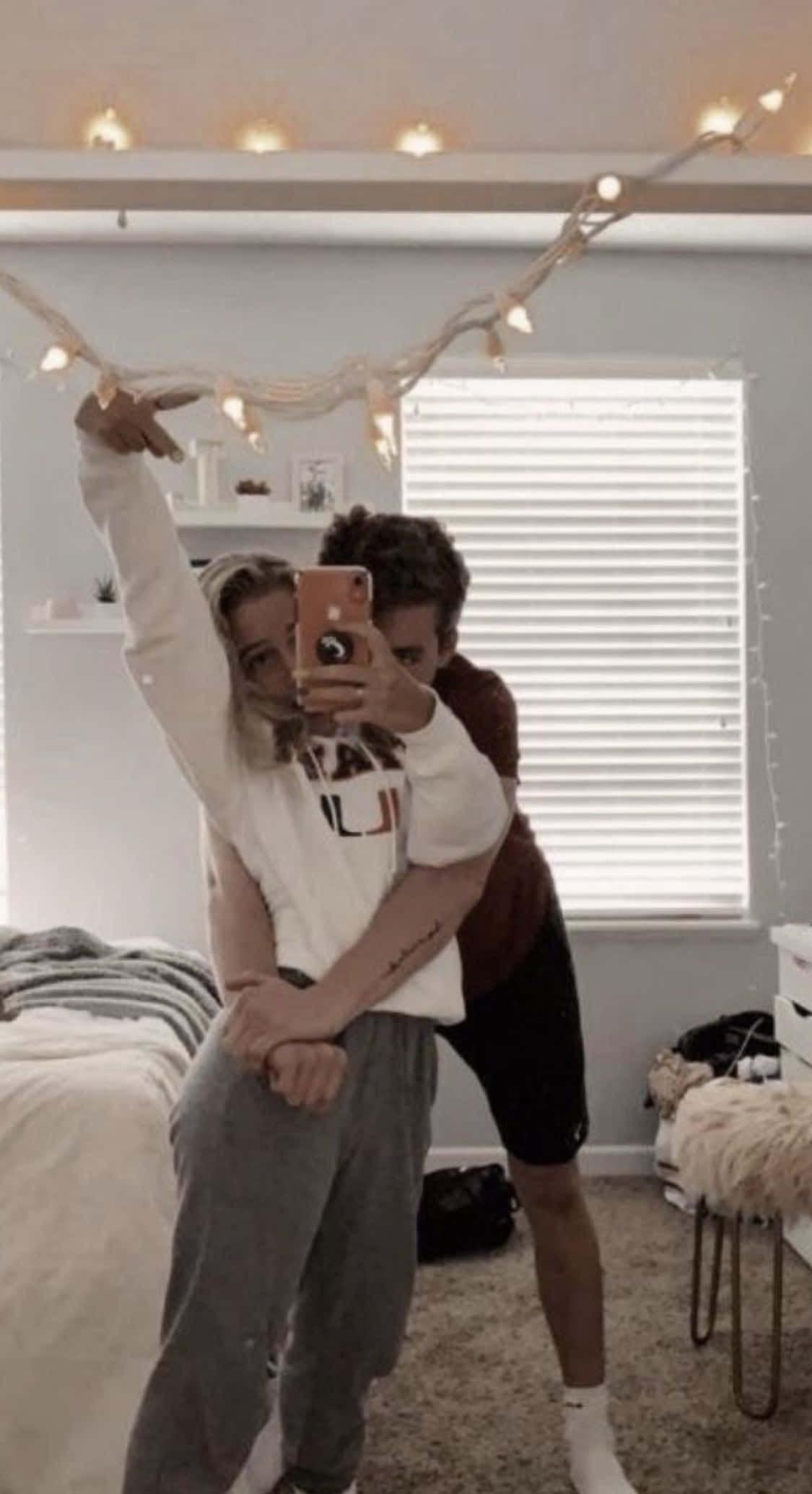 boyfriend 桌布 壁紙 — 兩個人在一個由串燈照亮的舒適臥室裡，一邊擺出俏皮的姿勢，一邊對著鏡子自拍。