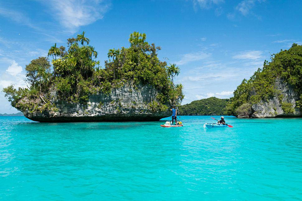 Micronesia 桌布 壁紙 — 兩個人在充滿活力的碧綠海水上划槳板和皮划艇，附近是鬱鬱蔥蔥的綠色石灰岩島嶼，在明亮的藍天下。