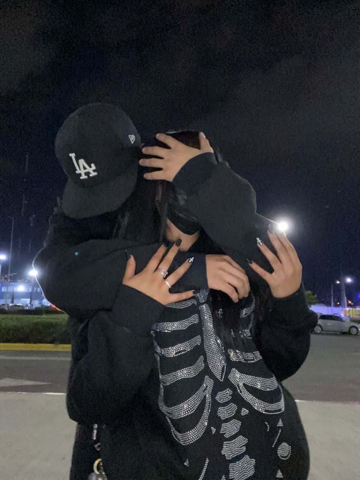 情侶 桌布 壁紙 — 兩個人在夜晚昏暗的停車場緊緊擁抱，一人戴著黑色LA帽，另一人穿著骷髏圖案上衣。