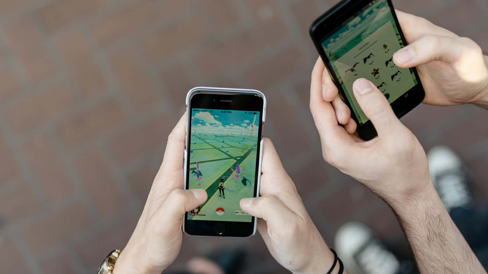 Pokemon Virtual World 桌布 壁紙 — 兩個人在戶外的磚砌路面上用智慧型手機玩Pokemon Go。