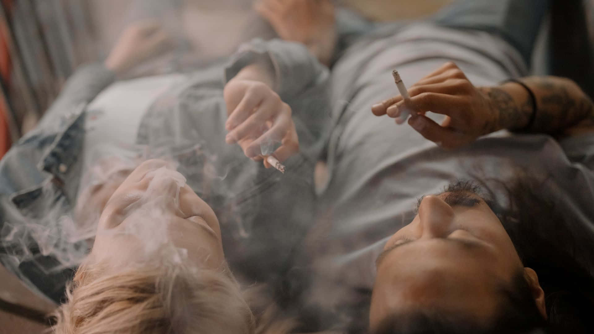 抽菸 桌布 壁紙 — 兩個人在昏暗的房間裡仰臥吸煙，煙霧在他們臉龐周圍繚繞。